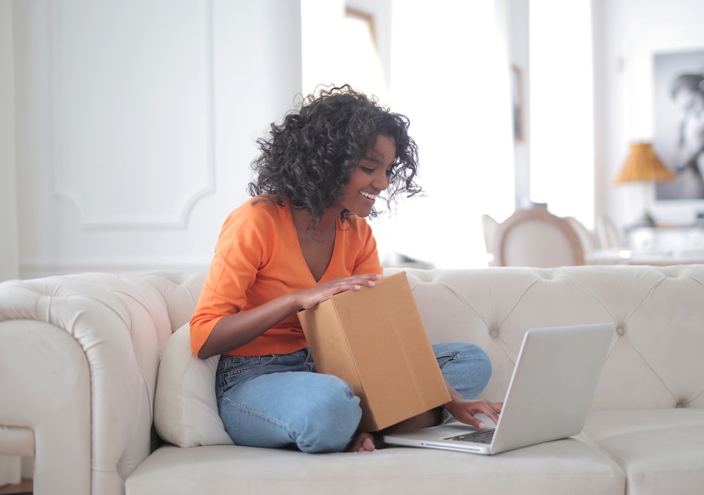 Happy woman retail customer with box browses protection plans on computer