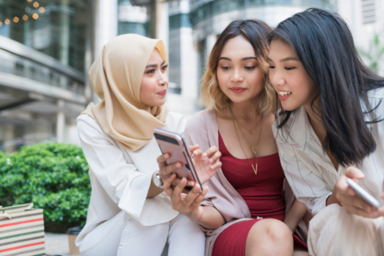 Three women customers are sitting in a shopping mall looking at a phone to follow national retail trends in 2022