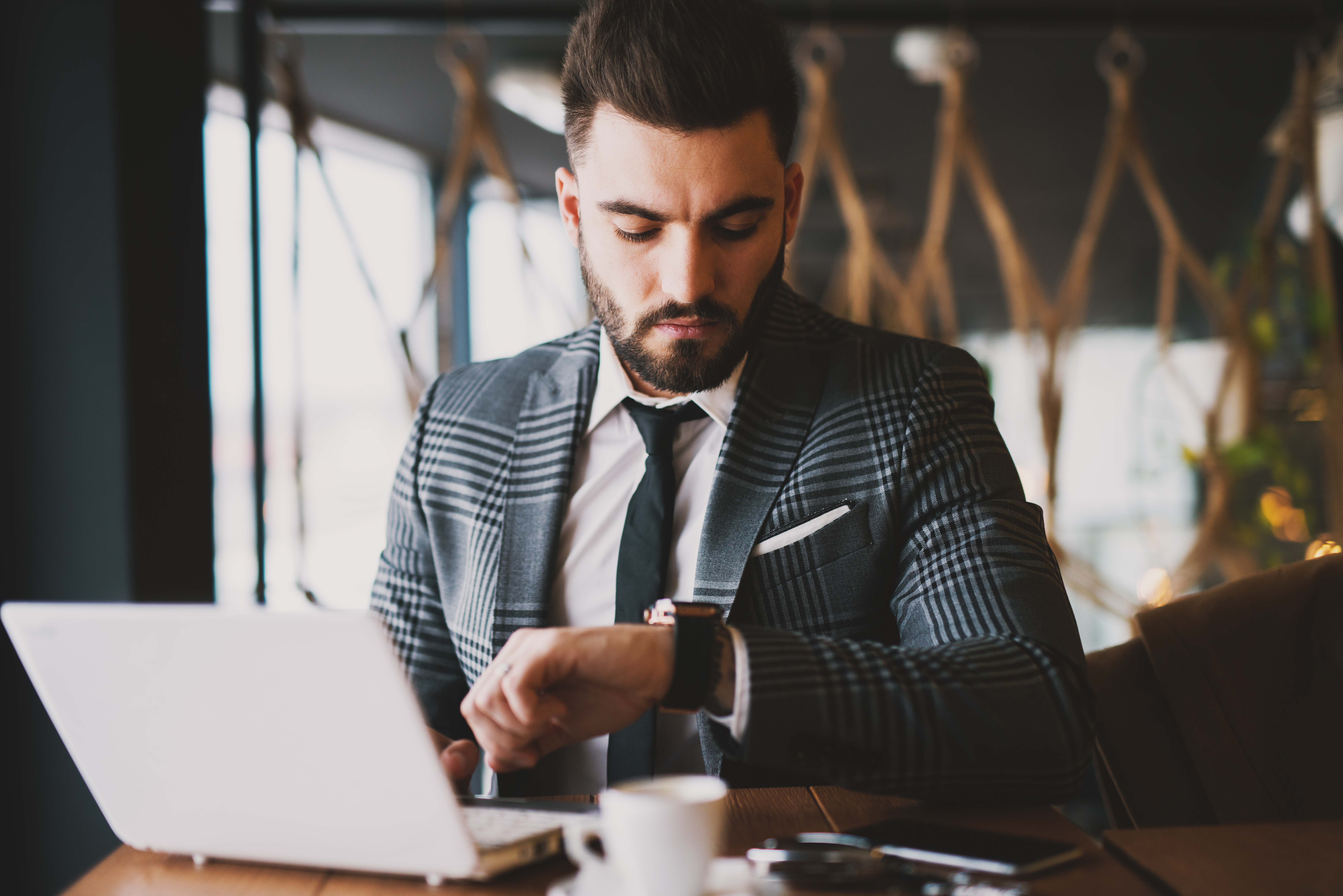 Man in a suit working on his laptop and checking his watch