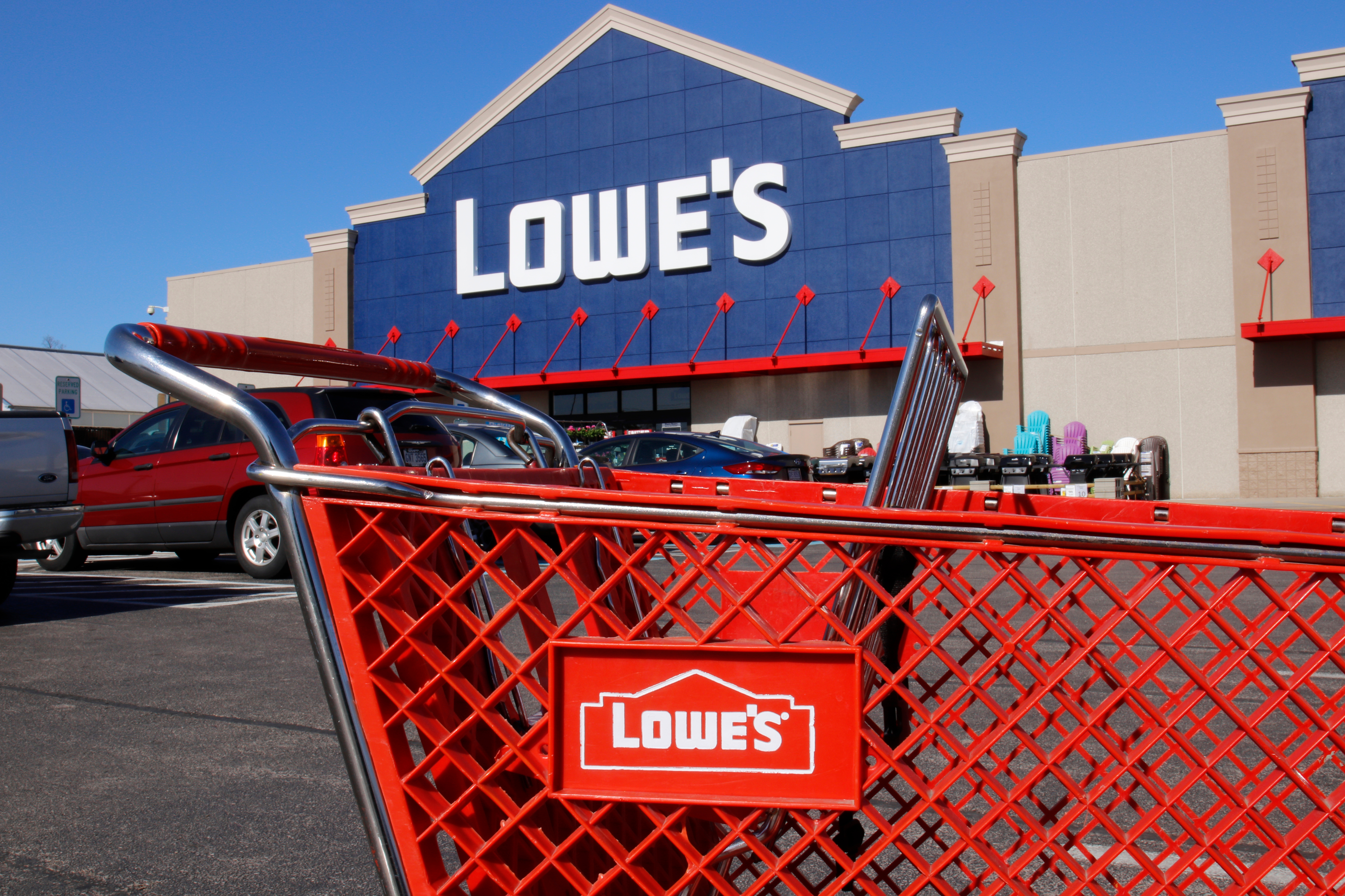 A red Lowe's shopping cart in front of a Lowe's storefront