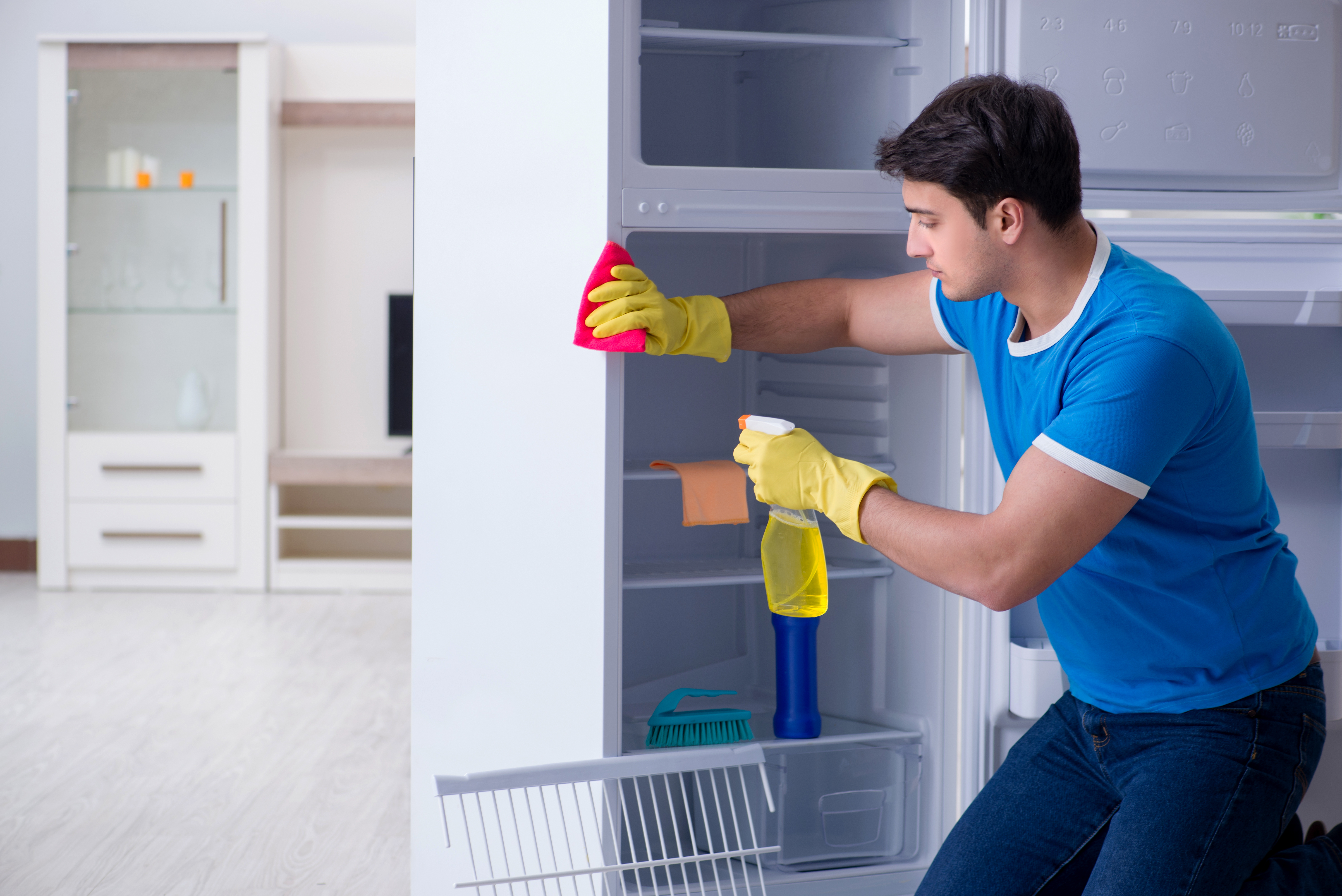 Man wearing blue shirt and yellow rubber gloves cleaning a refrigerator