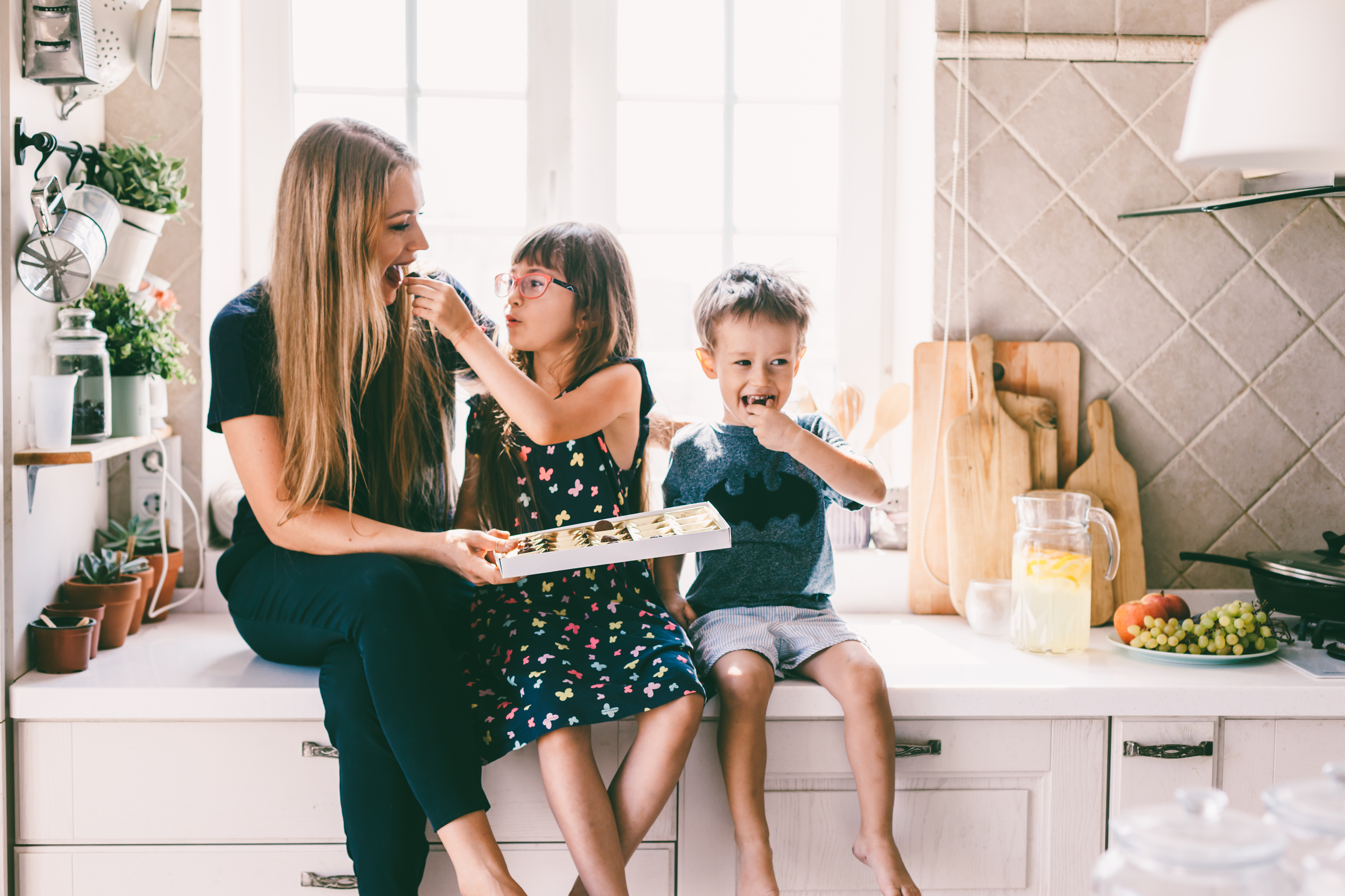 Woman and two kids sitting on the kitchen counter eating out of a snack box