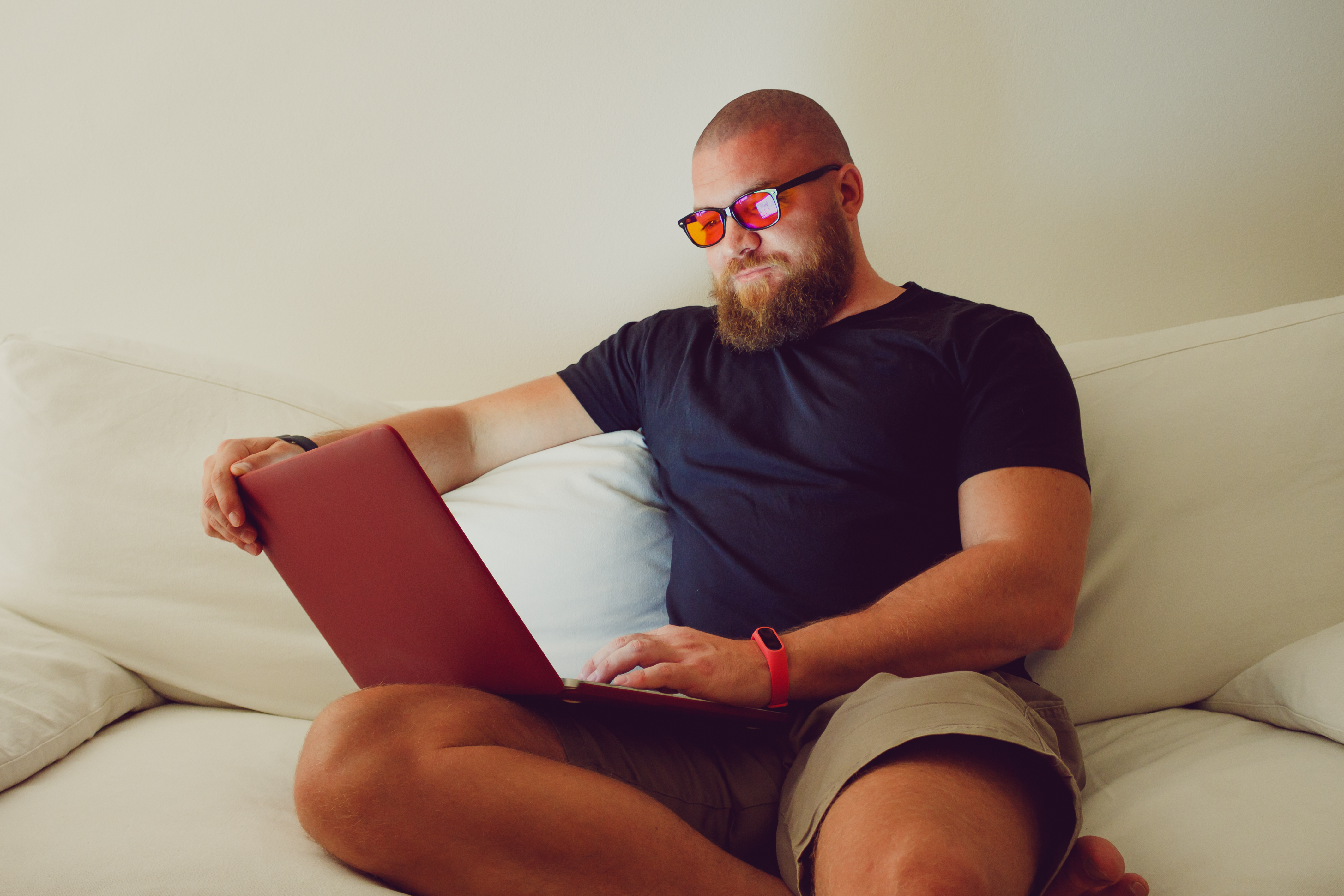 Man with beard sitting on couch using computer wearing blue light glasses