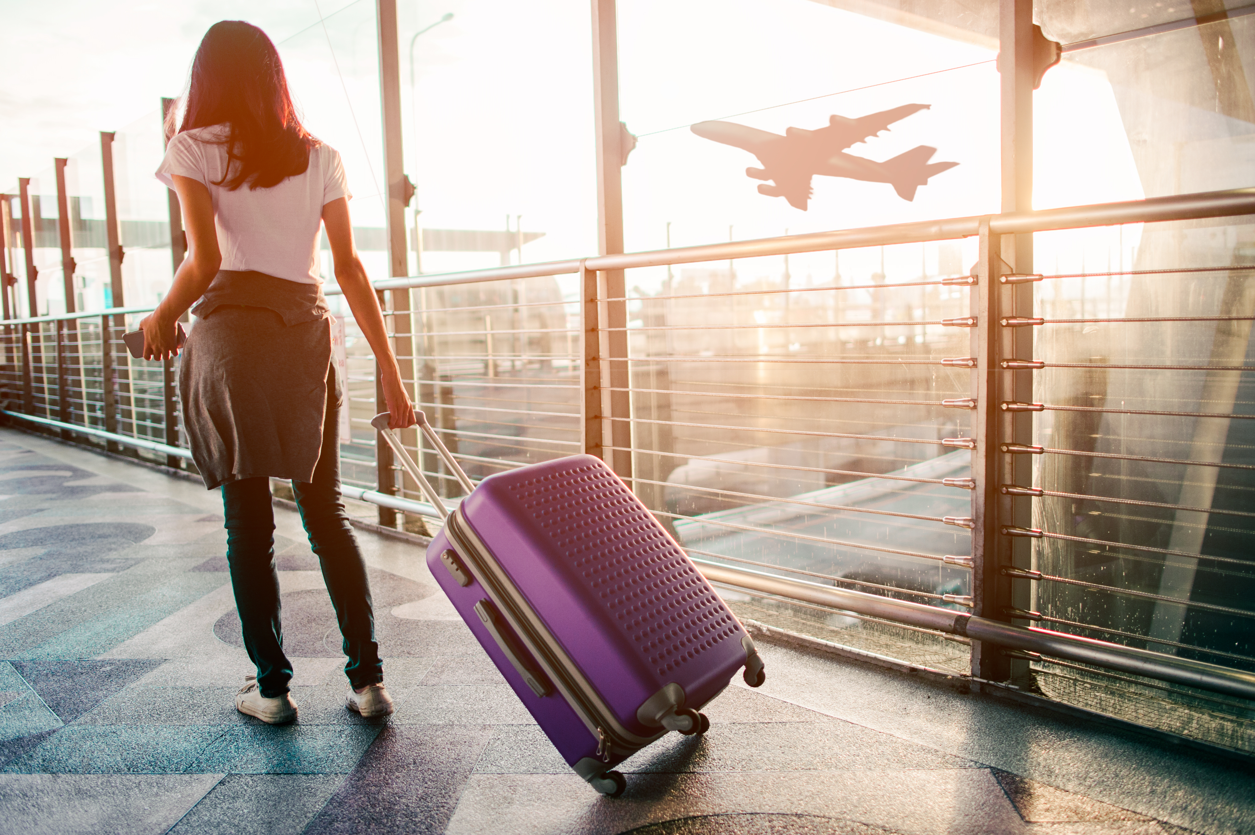 Woman walking through the airport with a purple rolling suitcase