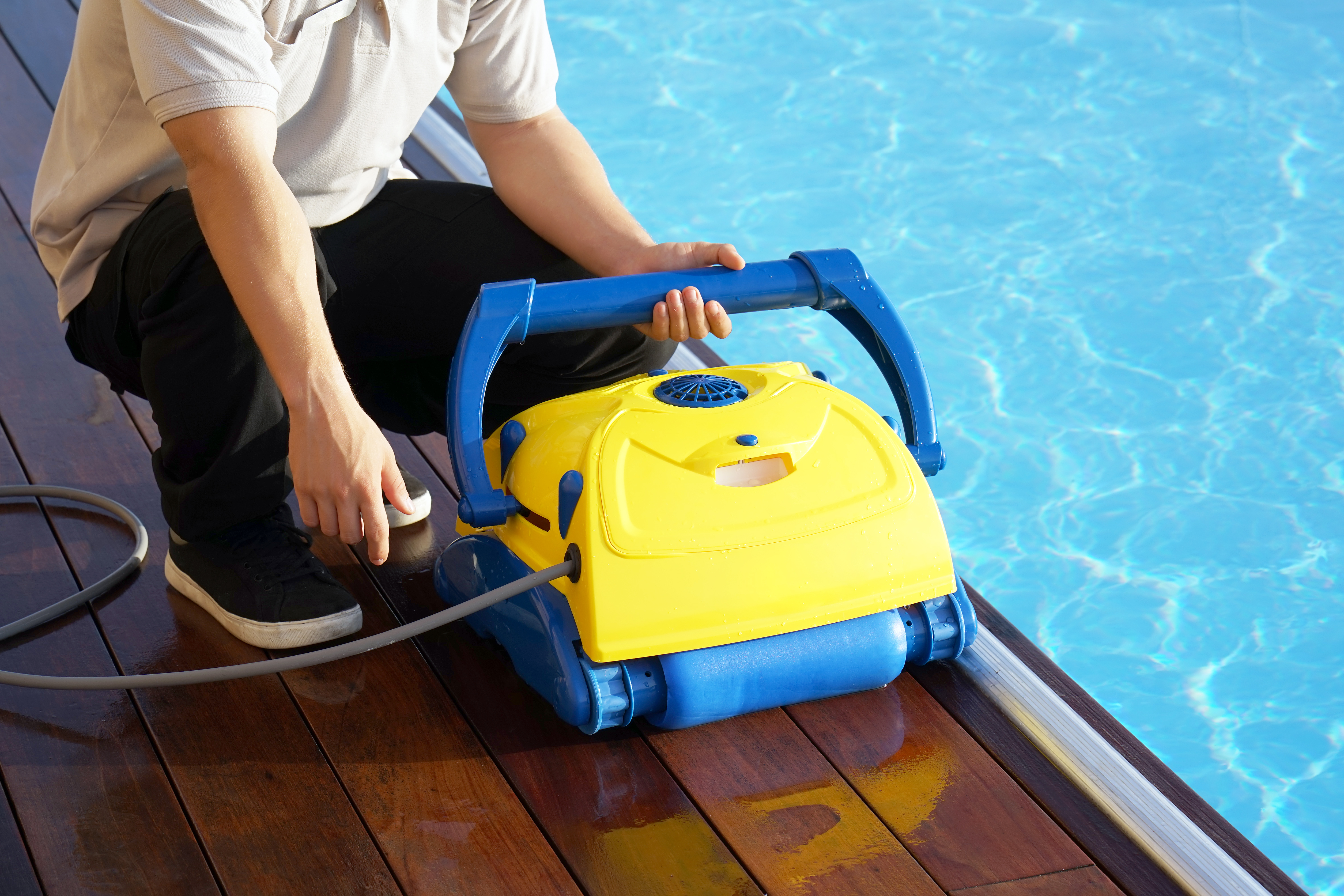 Person kneeling next to a pool holding a pool cleaning robot