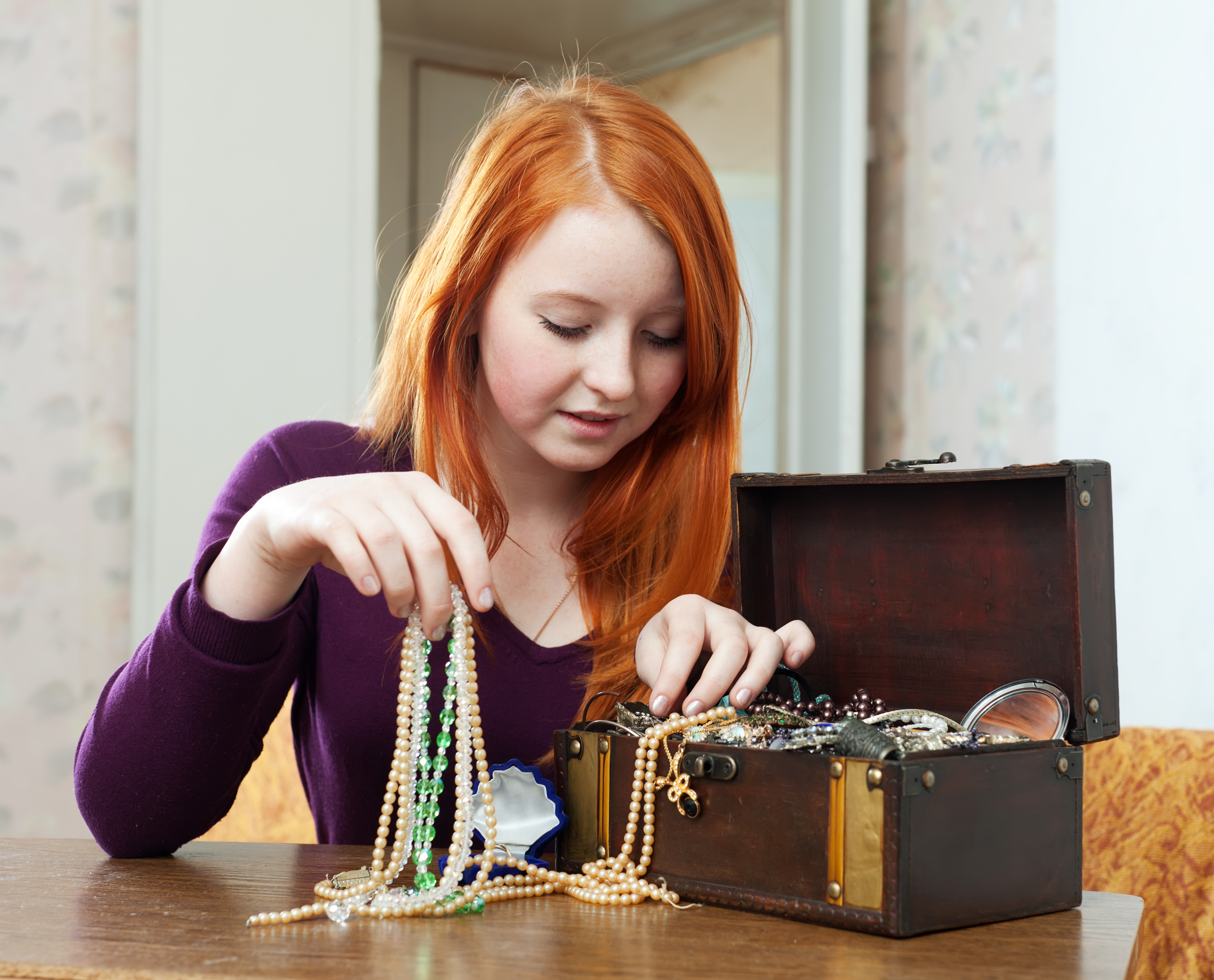 Girl wearing a purple shirt sitting at a table going through a jewelry box