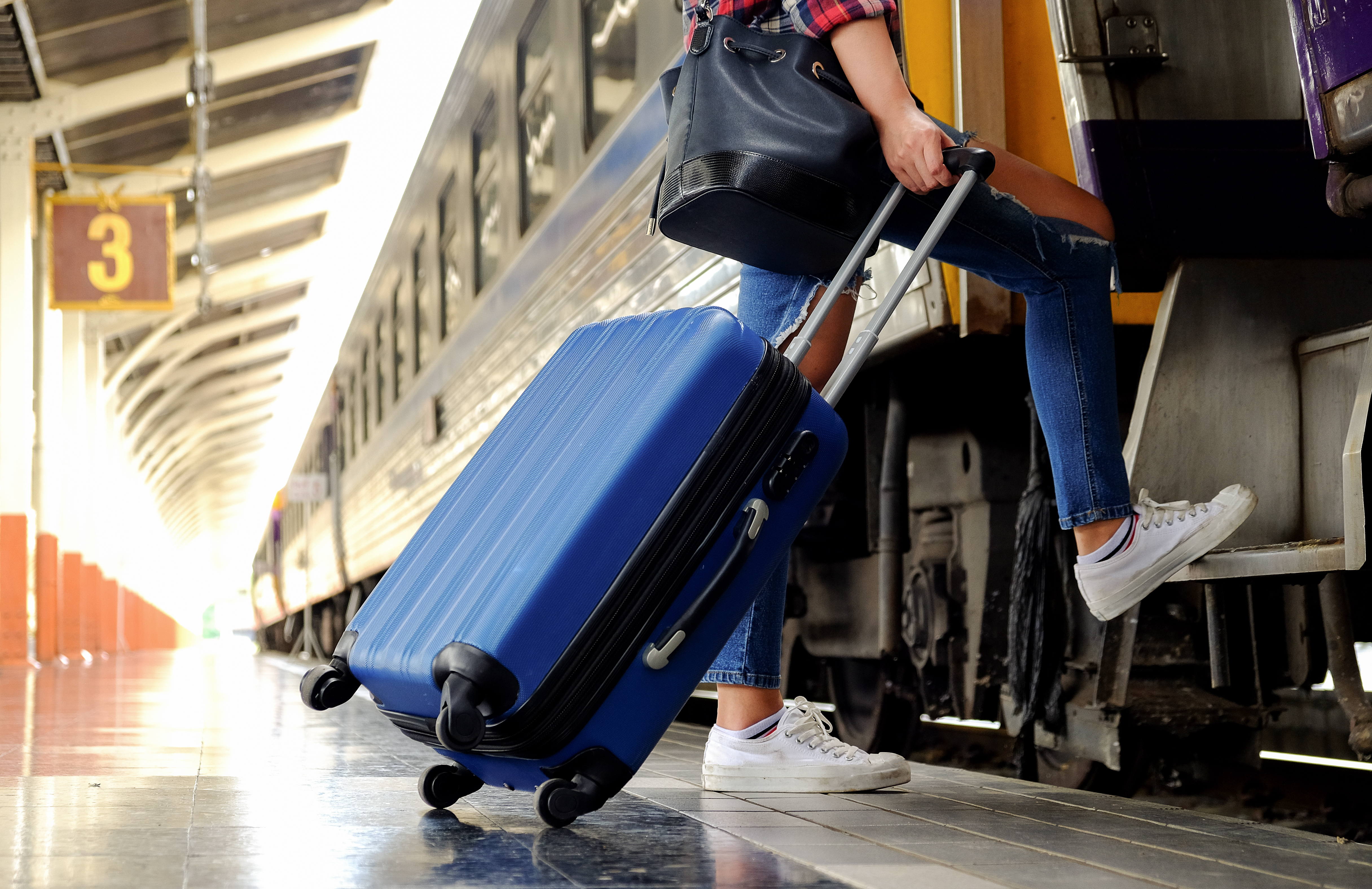 person boarding train with suitcase and bag