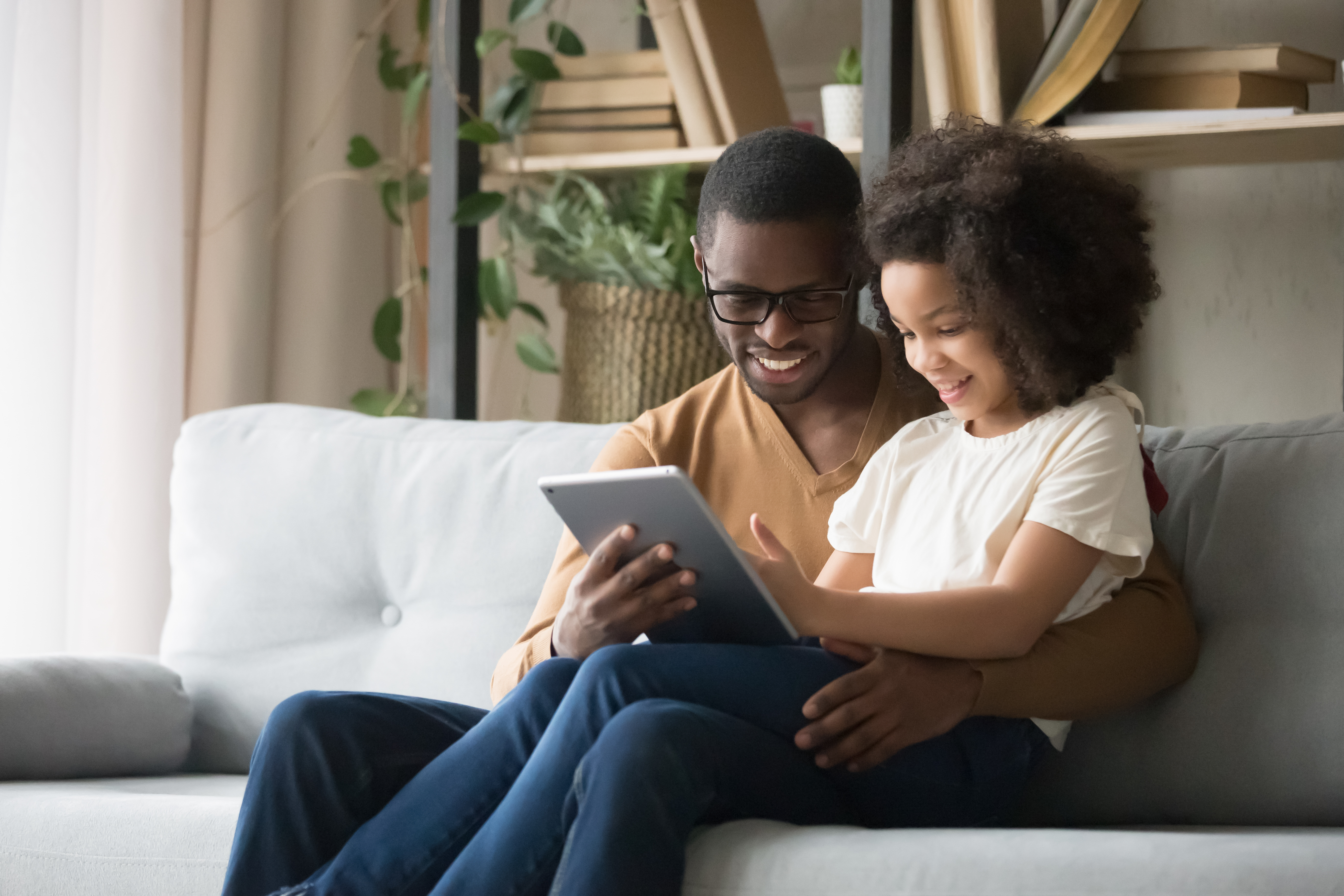 Father and his daughter sitting on the couch using an iPad