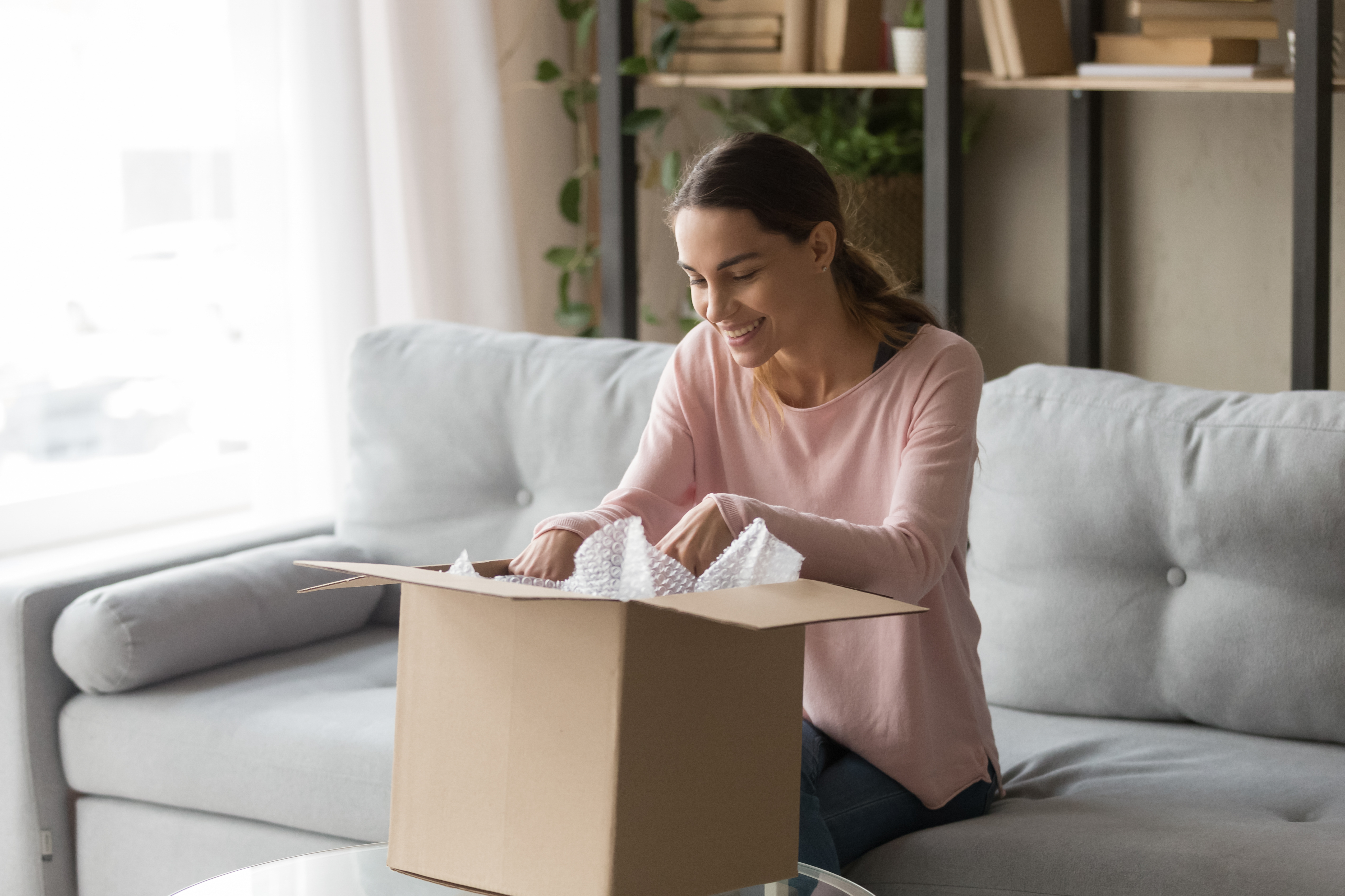 Woman in a pink shirt smiling and opening a cardboard box