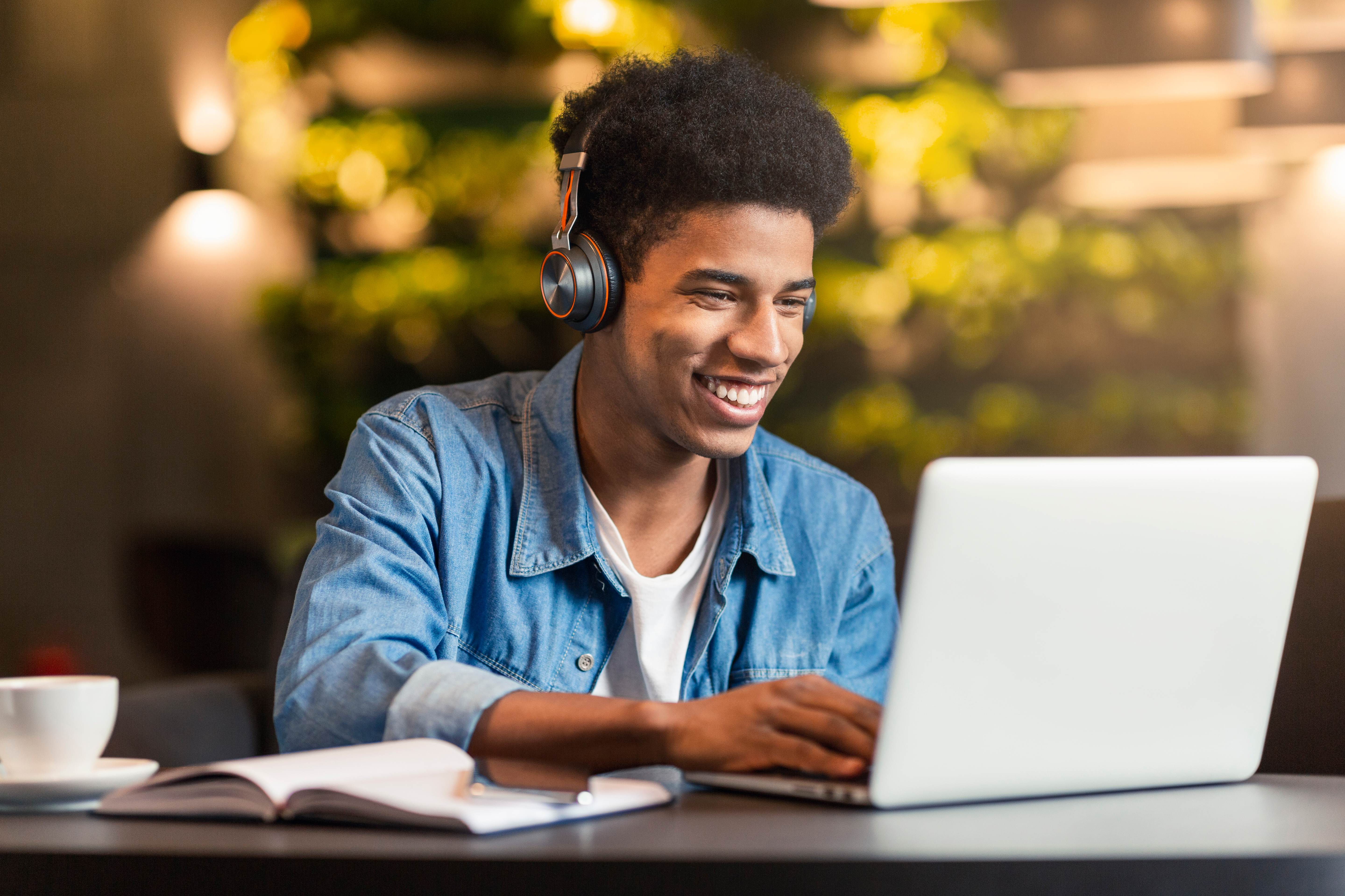 Young man wearing wireless headphones looking at his laptop and smiling