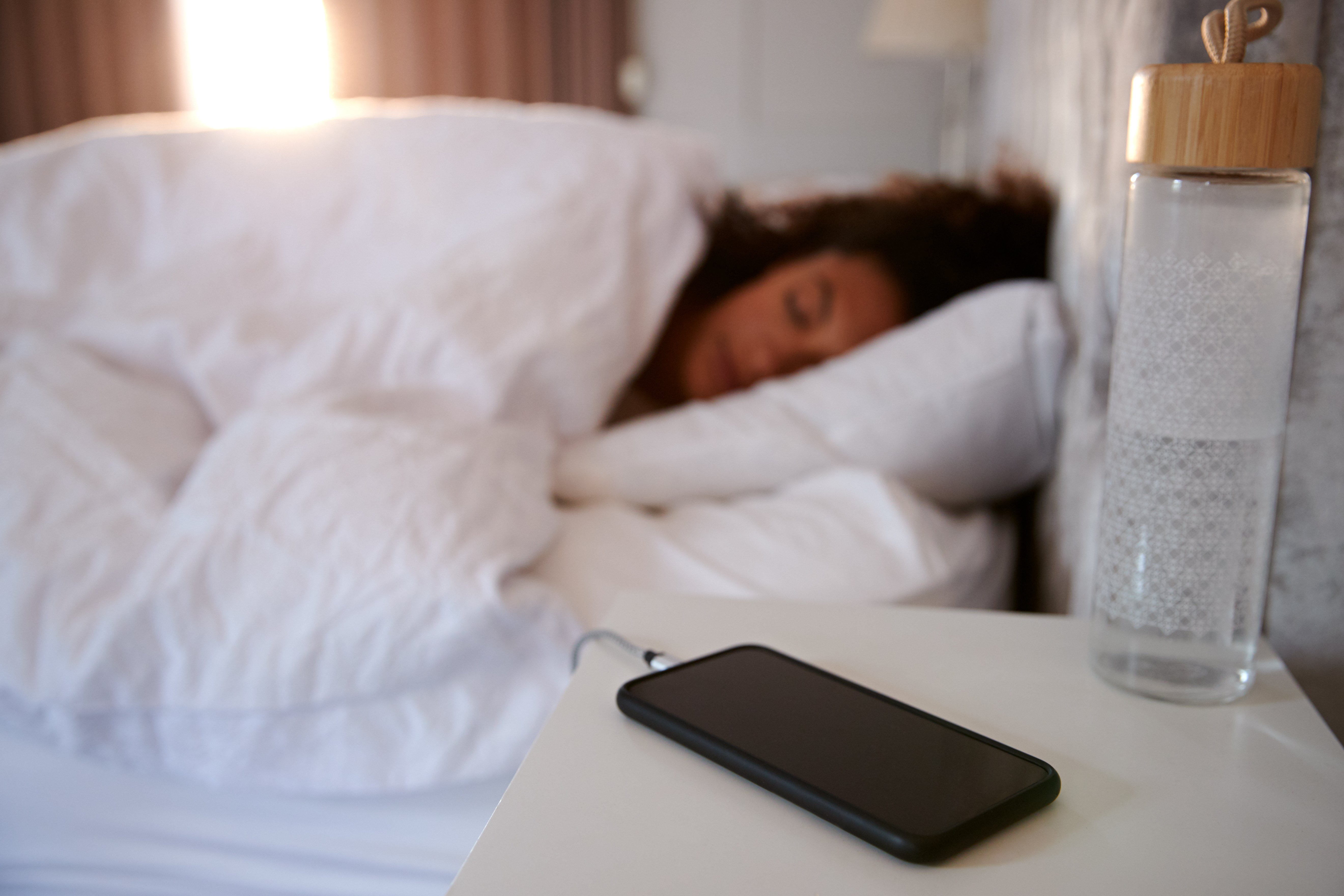 Woman asleep in bed with her phone on the bedside table