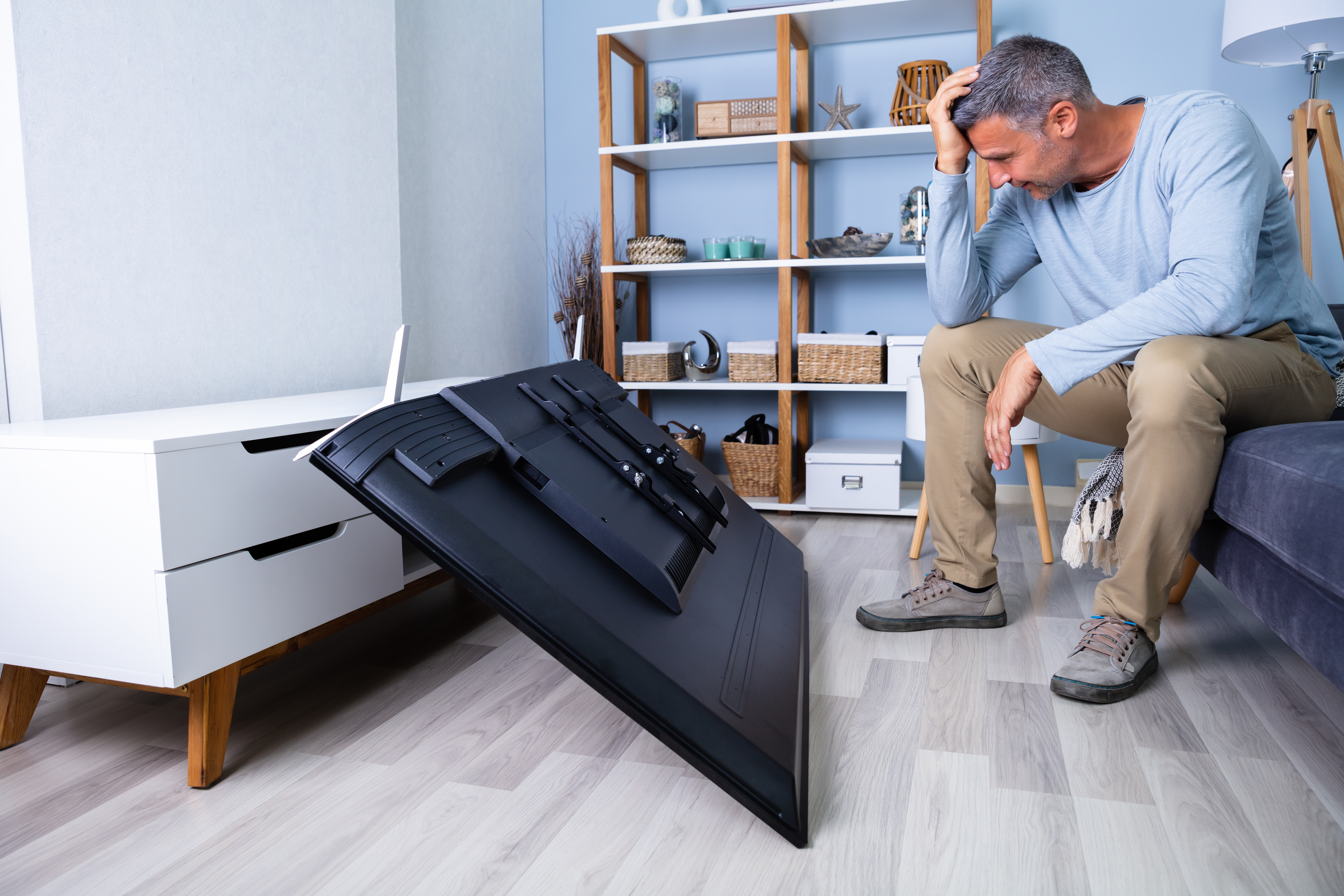 Man with head in his hands looking at a TV that's fallen over
