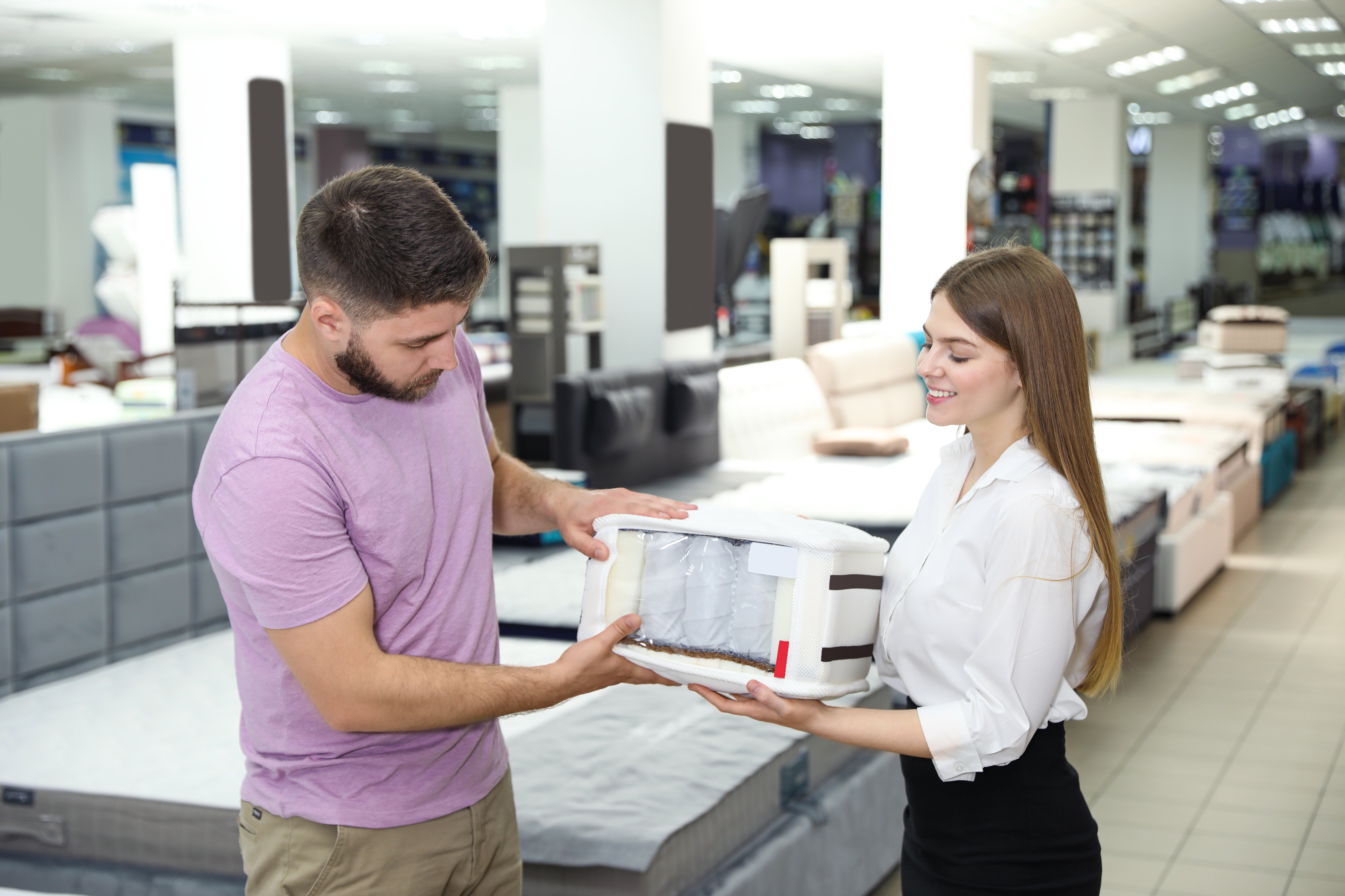 Man wearing a purple shirt looking at a mattress sample in a showroom