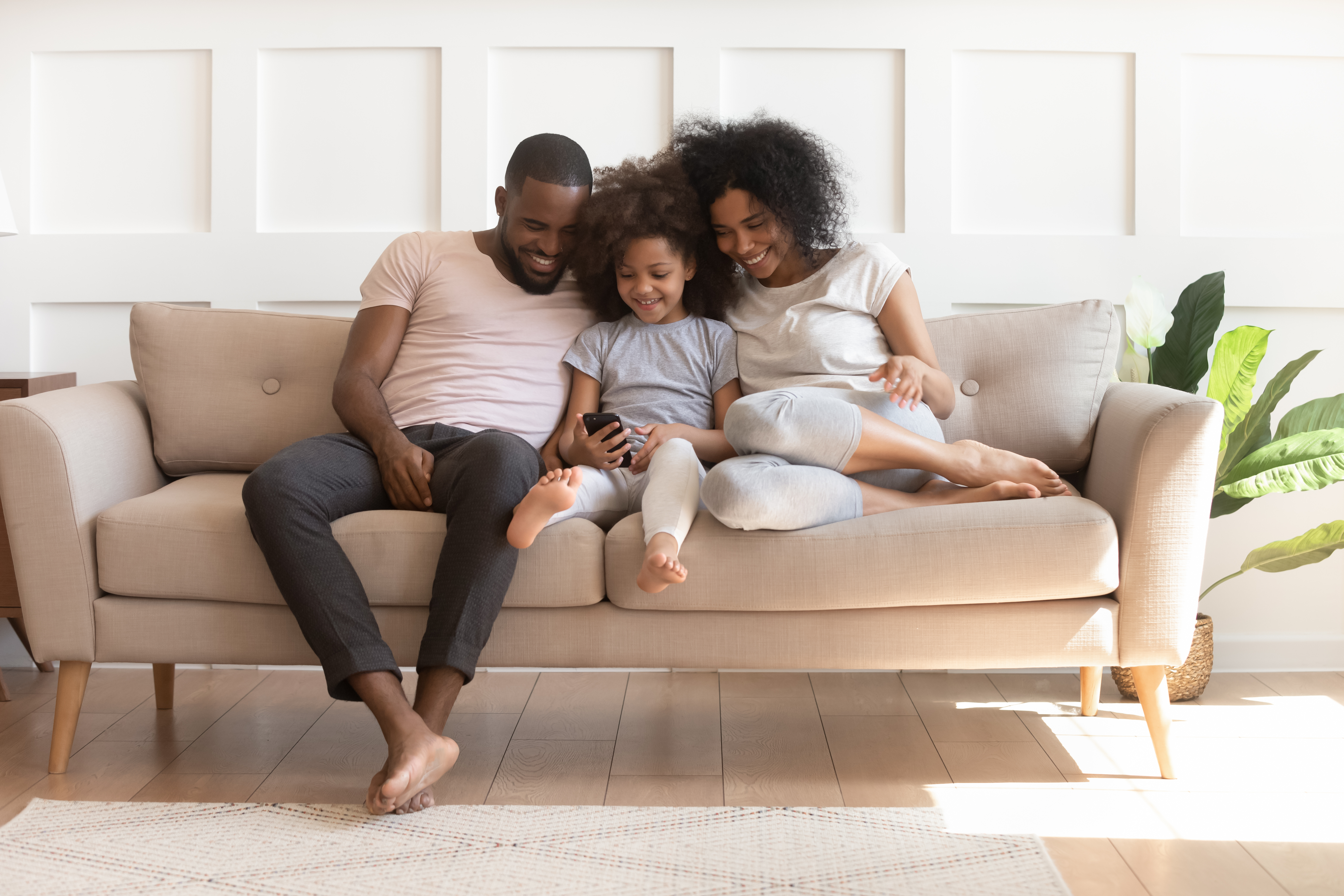 Family sitting together on a beige couch looking at a smartphone