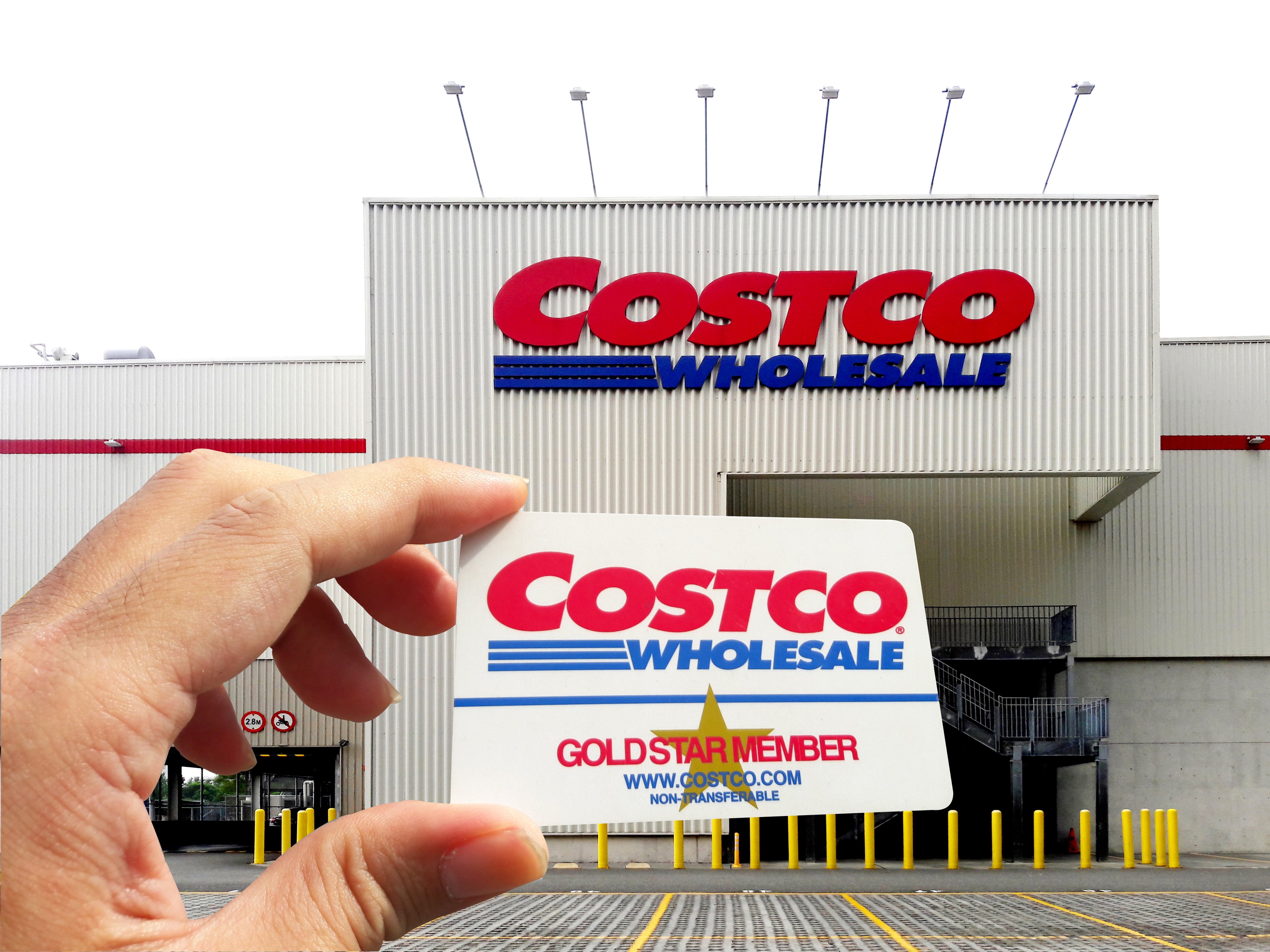 Person holding up a Costco membership card in front of Costco store