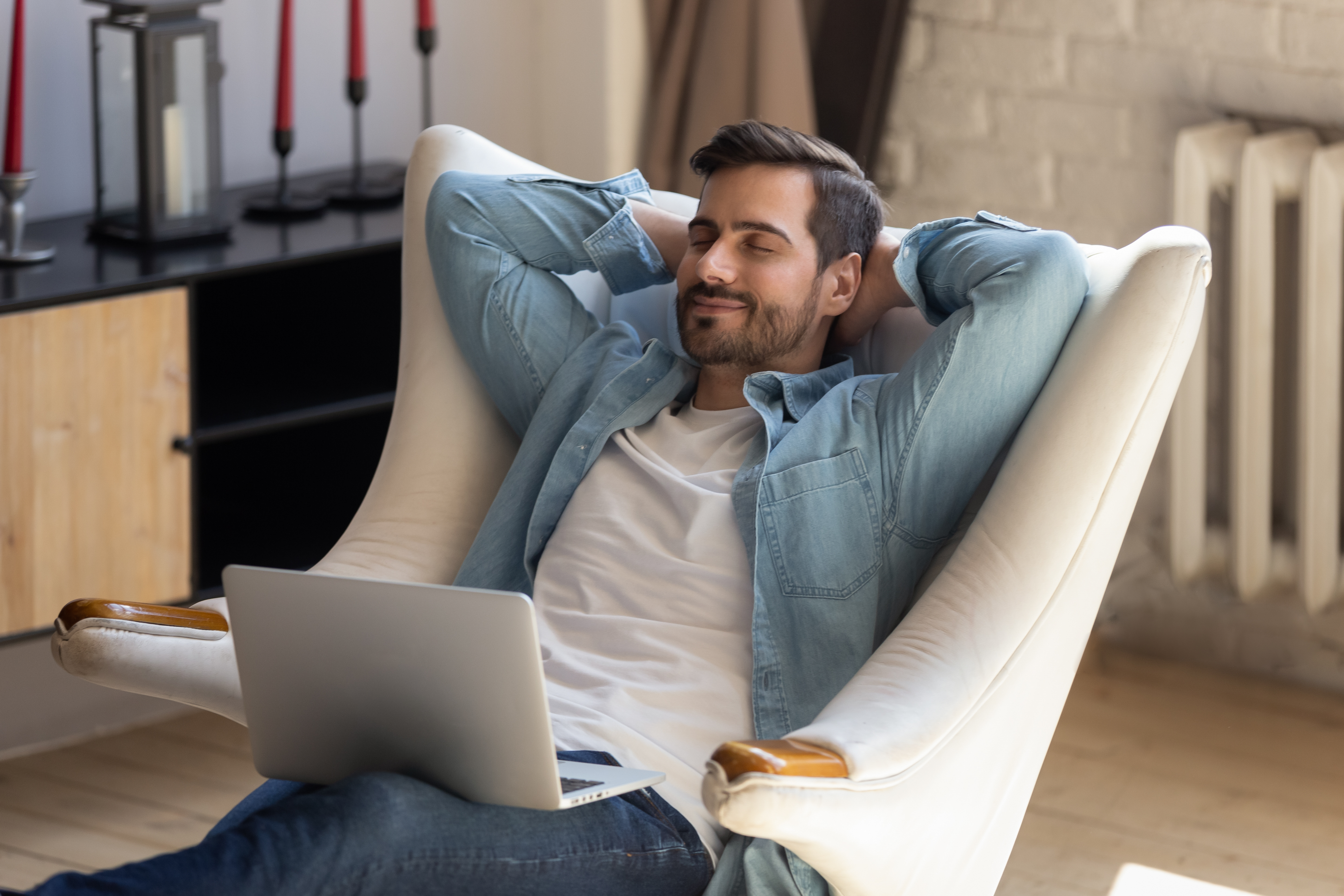 Man with a laptop in his lap leaning back in his chair smiling