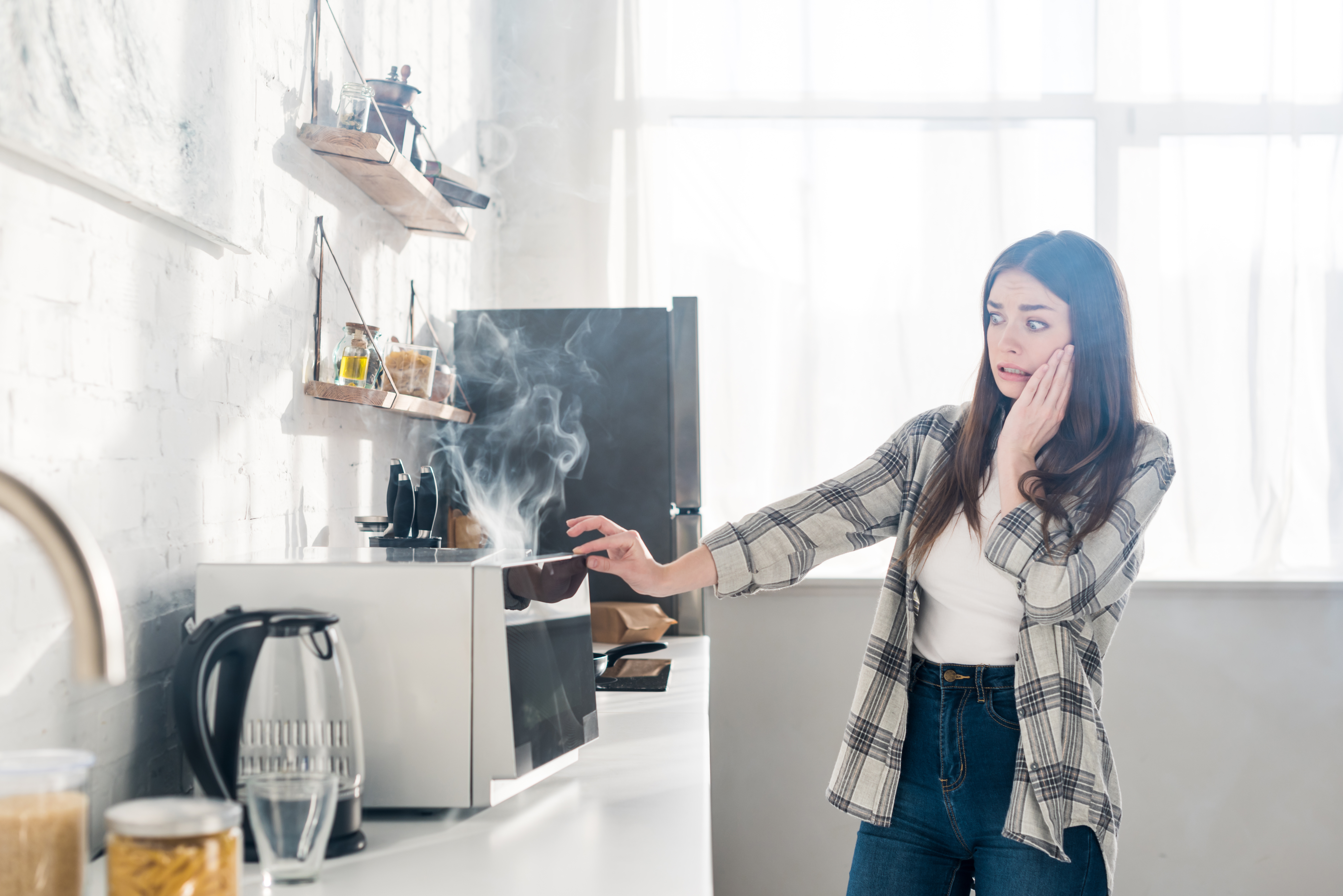 Woman looking afraid at a smoking microwave