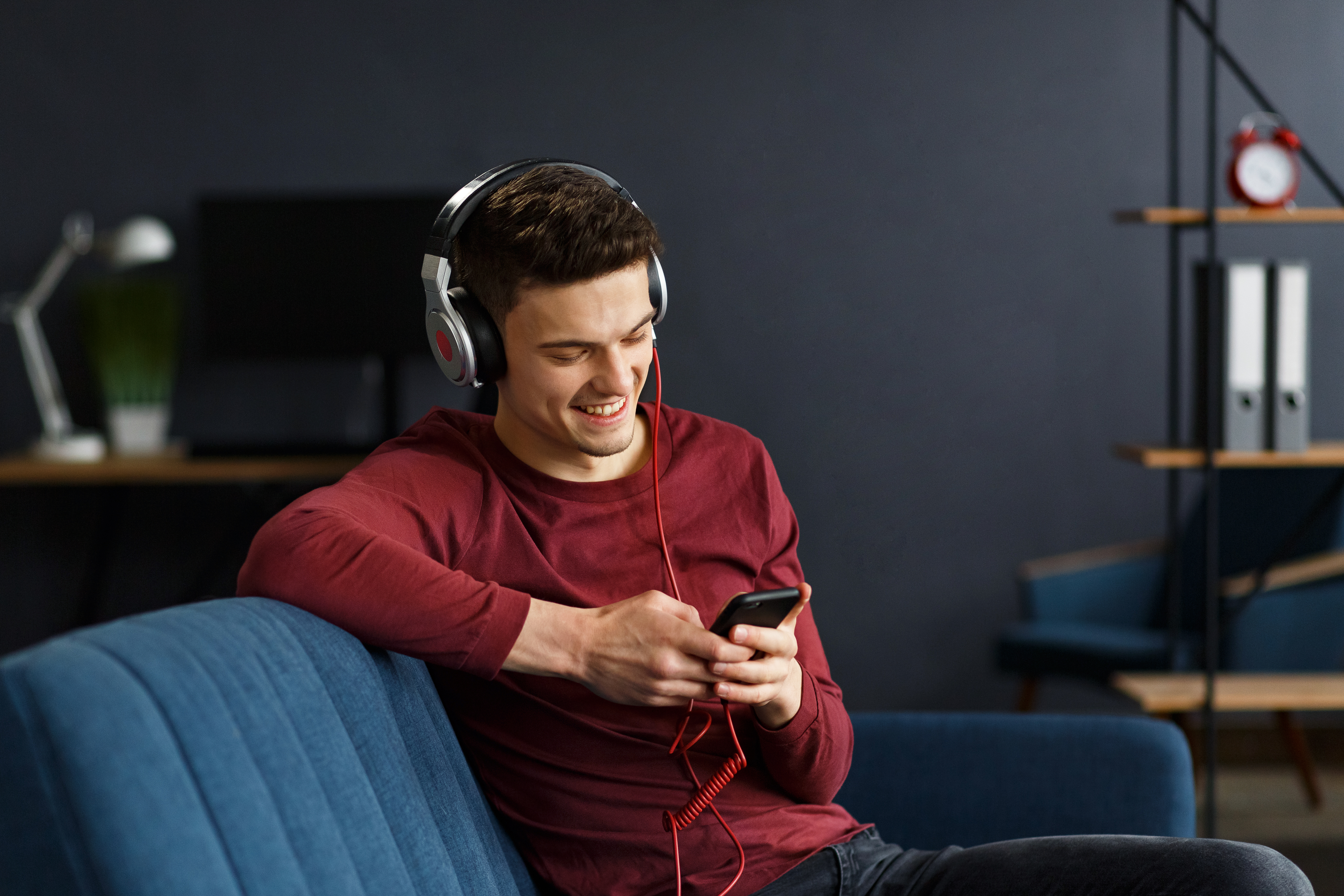 Man wearing a red shirt sitting on a couch listening to music with headphones on