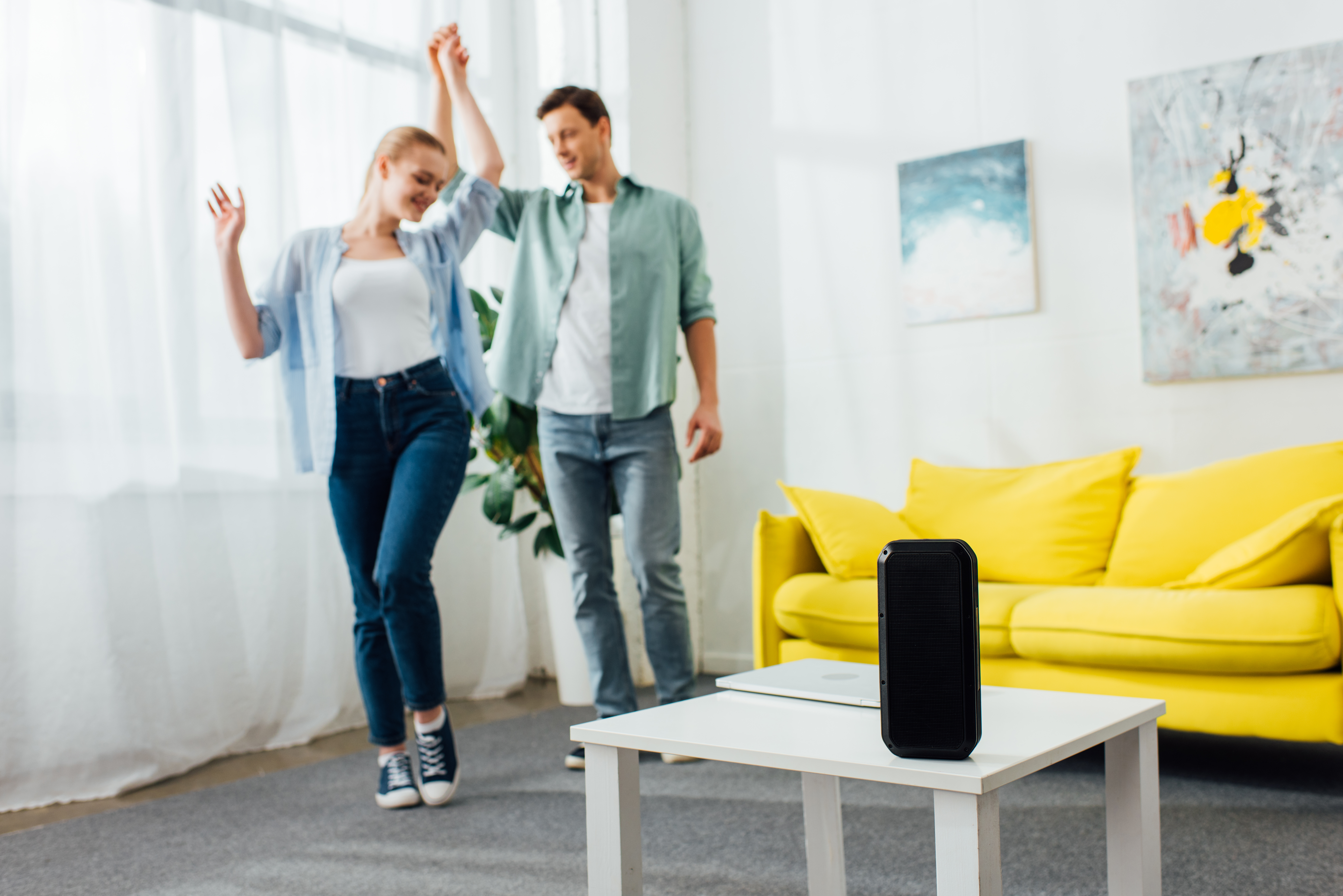 Couple dancing to music in their living room with a speaker playing on the coffee table