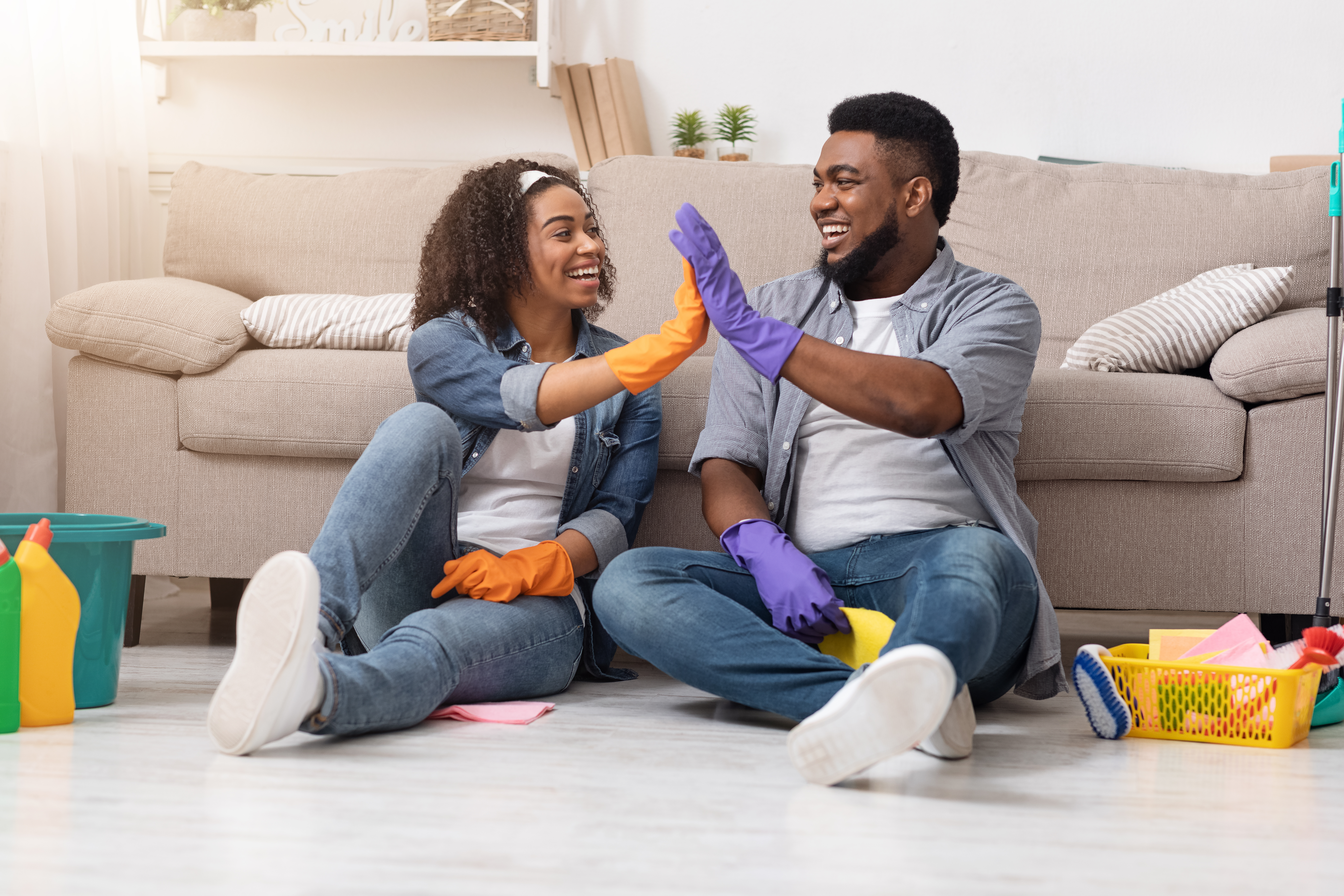 Man and woman high-fiving each other with cleaning products on the floor around them