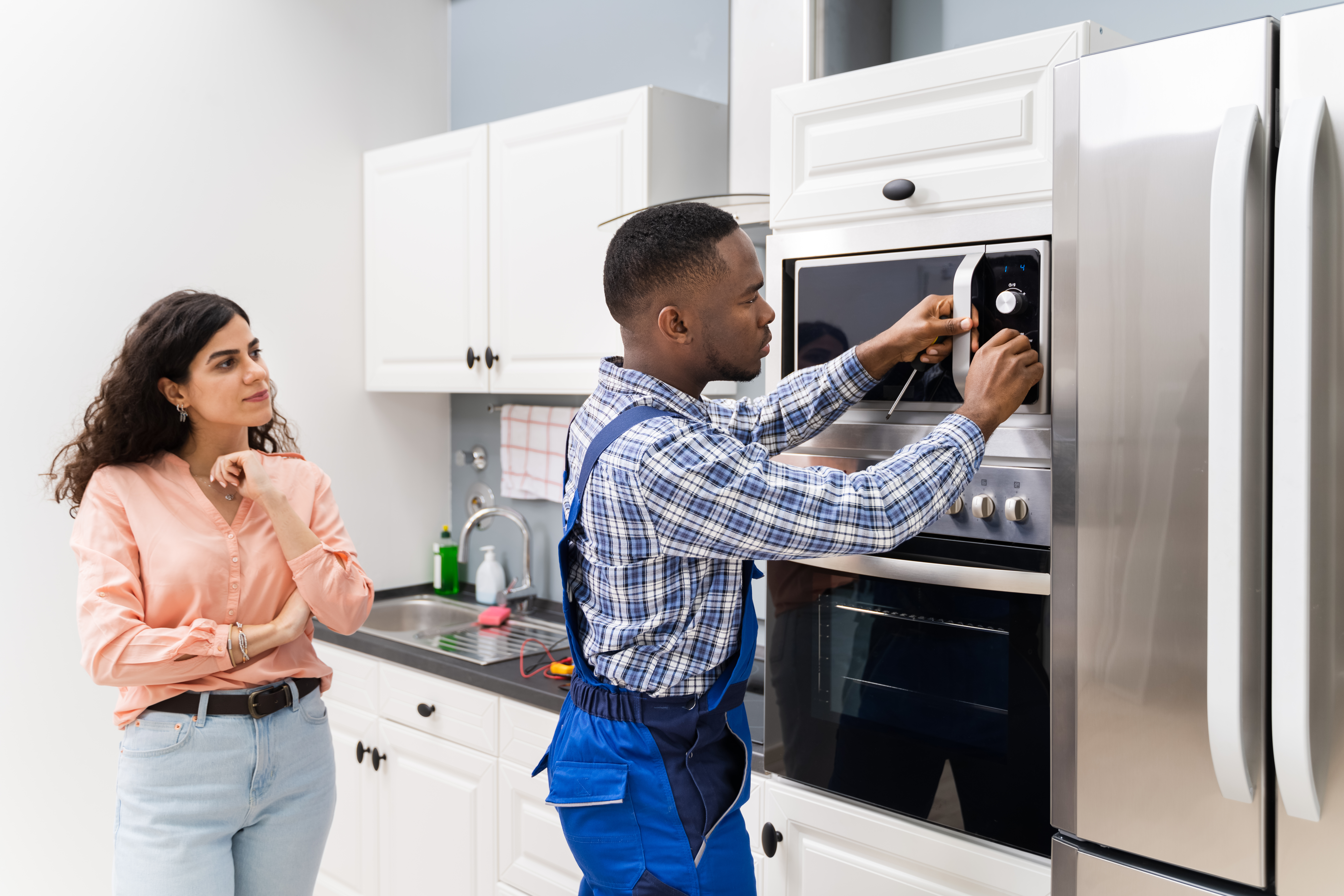 Man repairing a microwave while a woman looks on