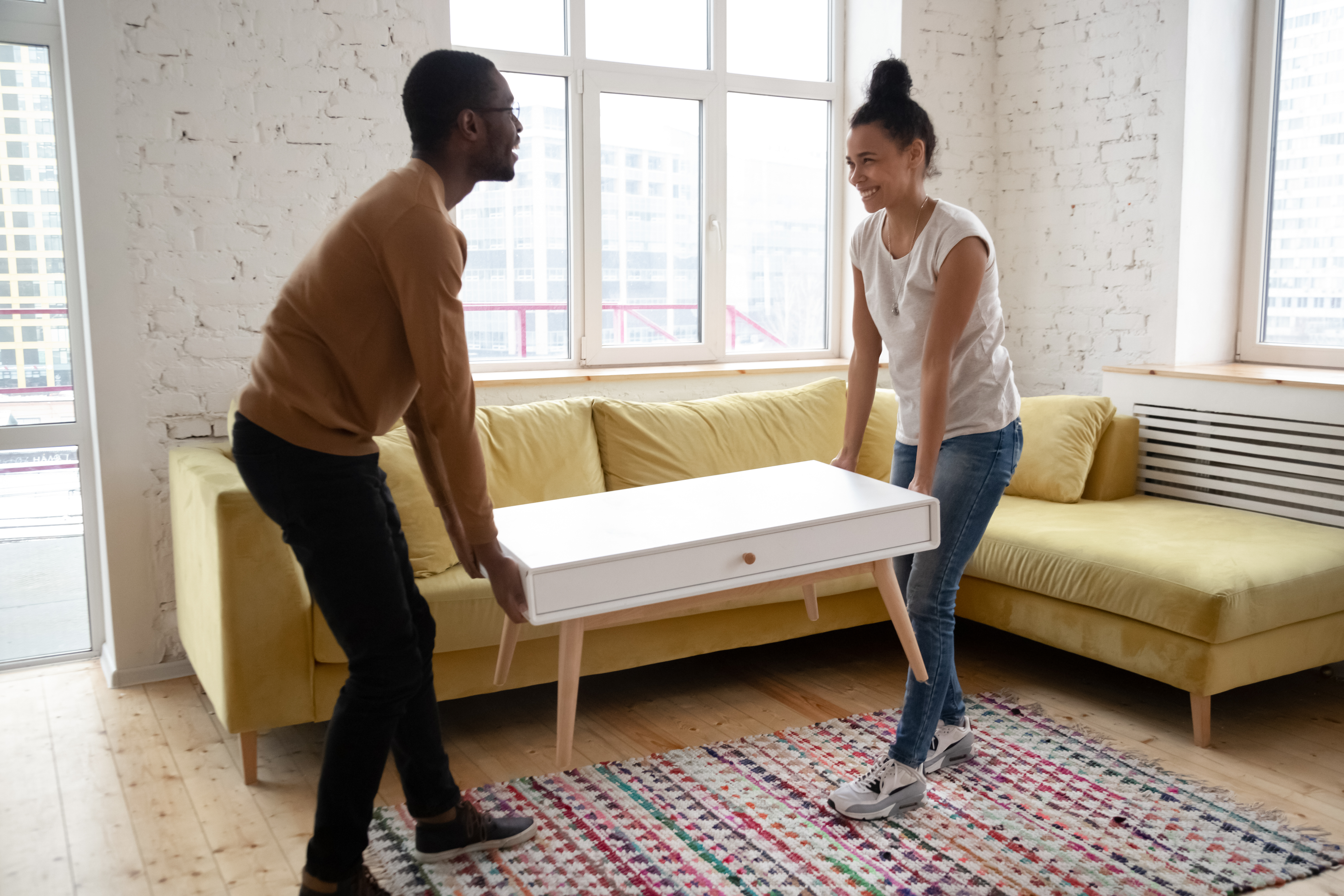 Man and woman smiling moving a coffee table into a living room