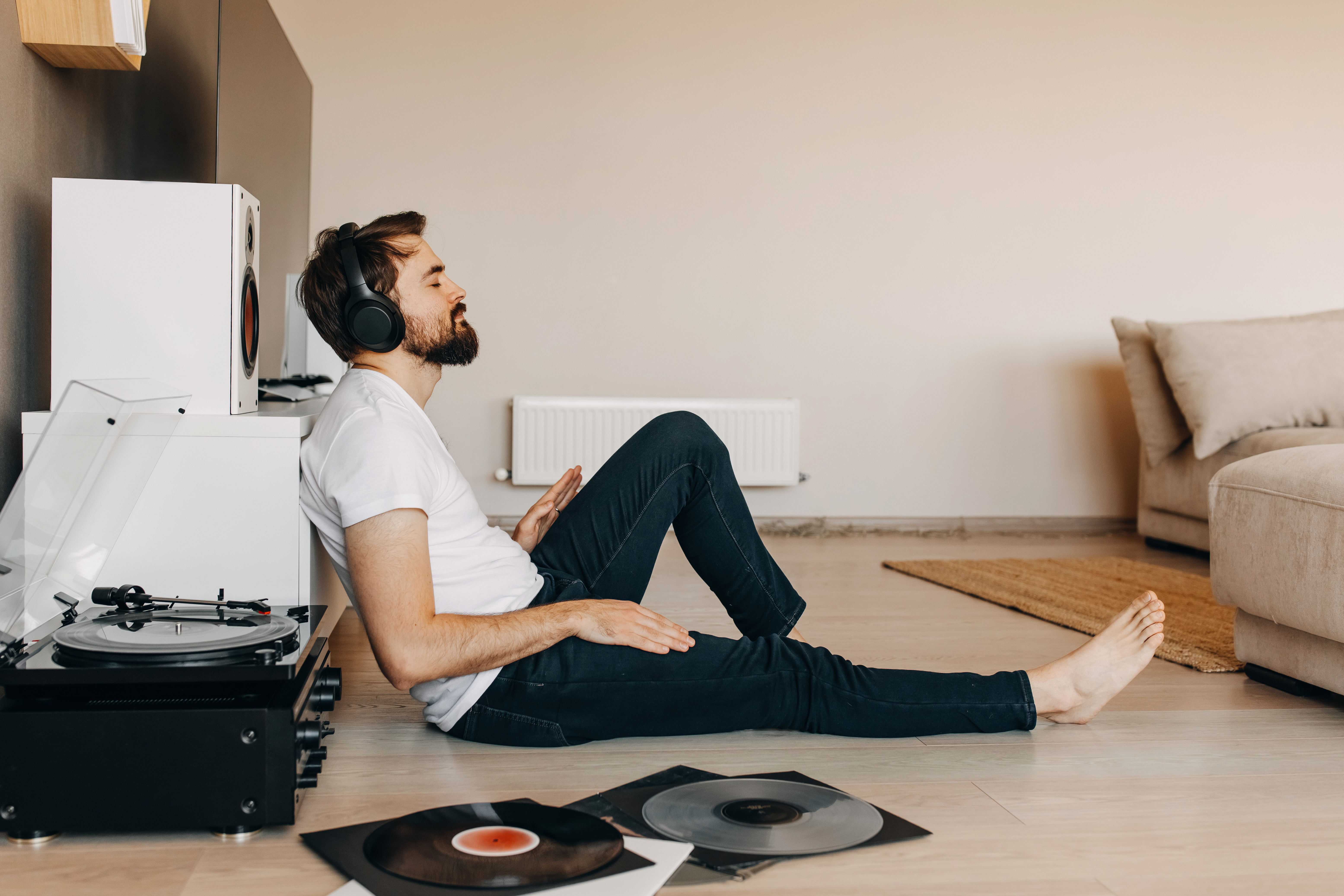 Man sitting on the ground wearing headphones and listening to music on a record player