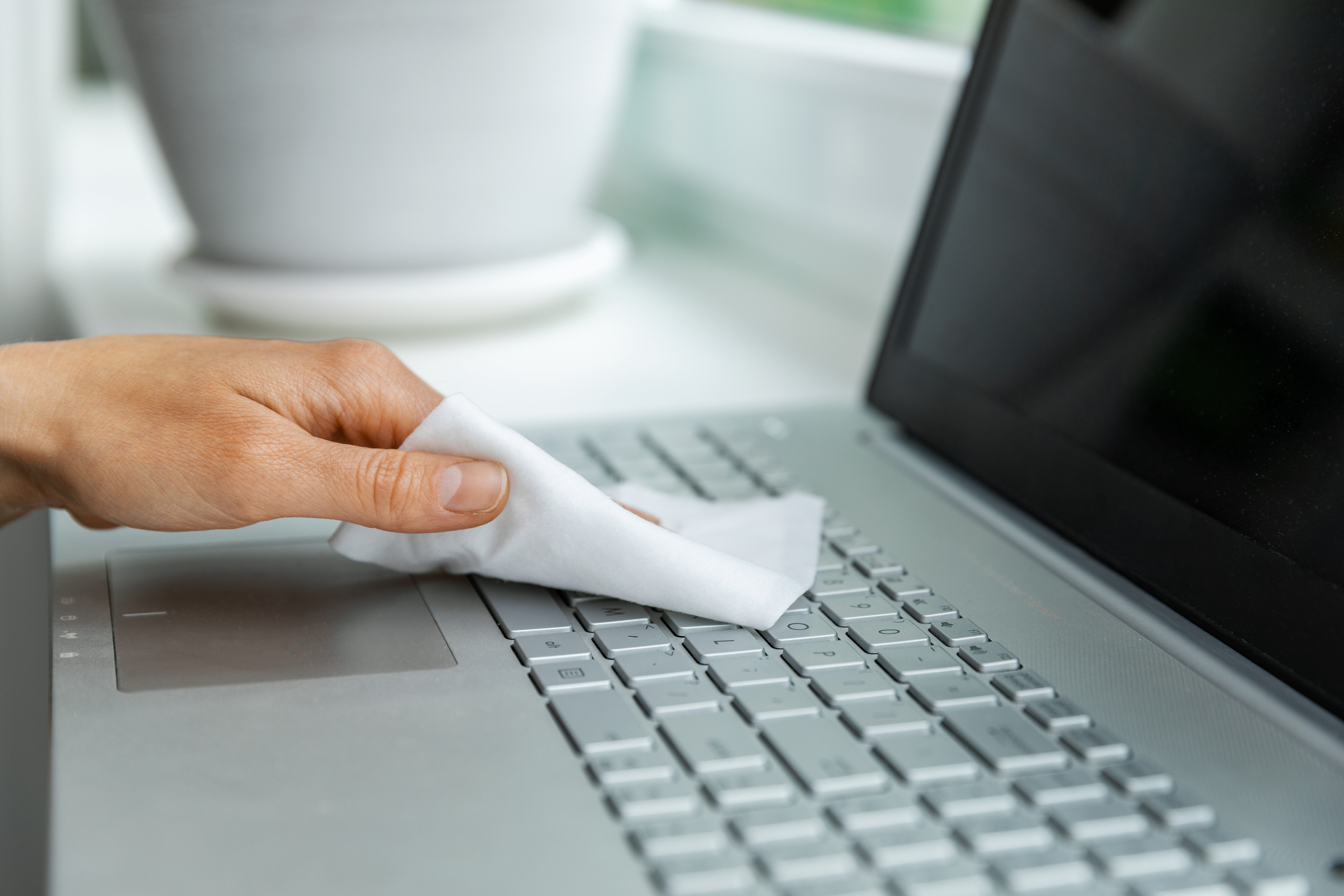 Person using a cloth to wipe down a laptop keyboard