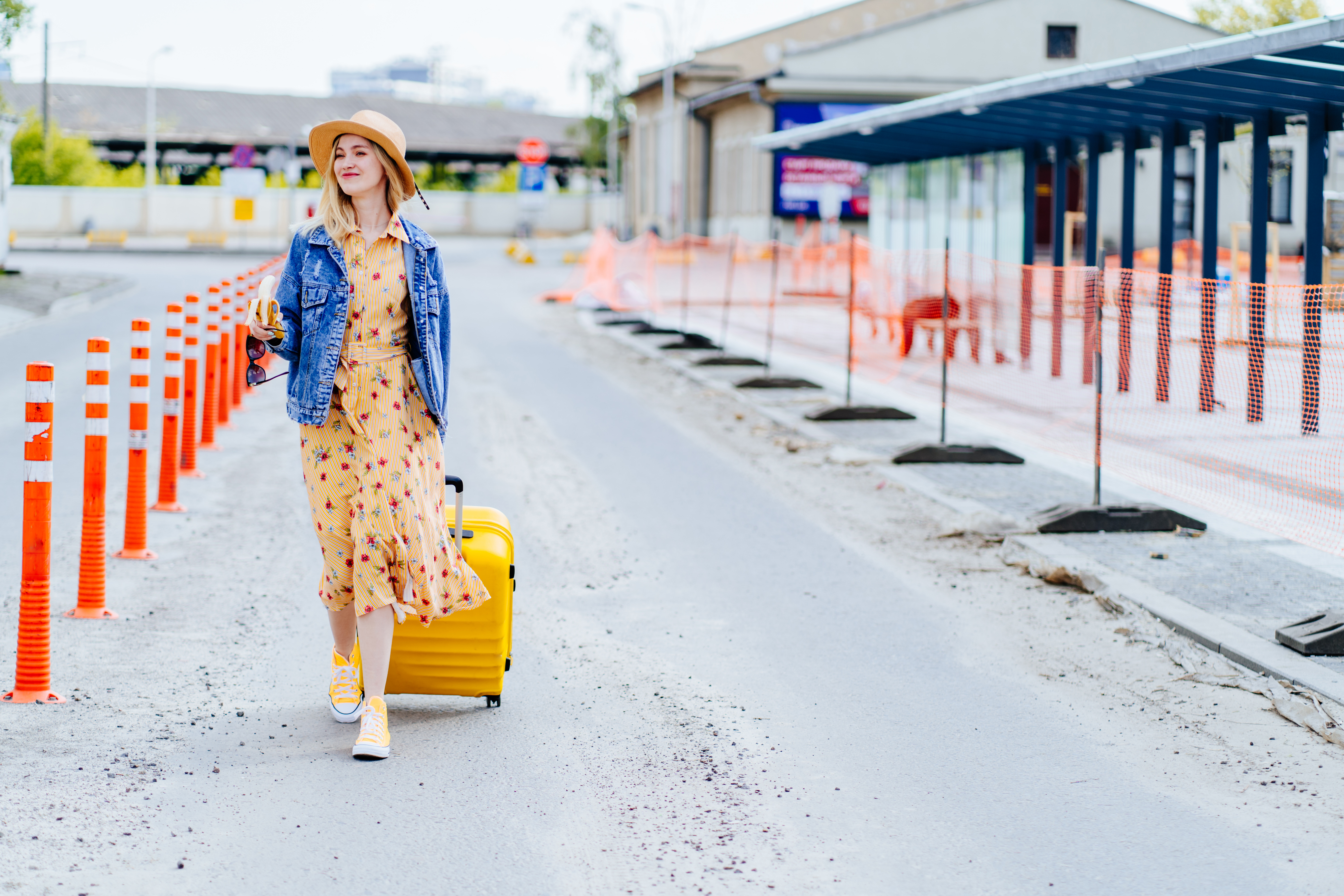 Woman with a yellow suitcase walking down a street