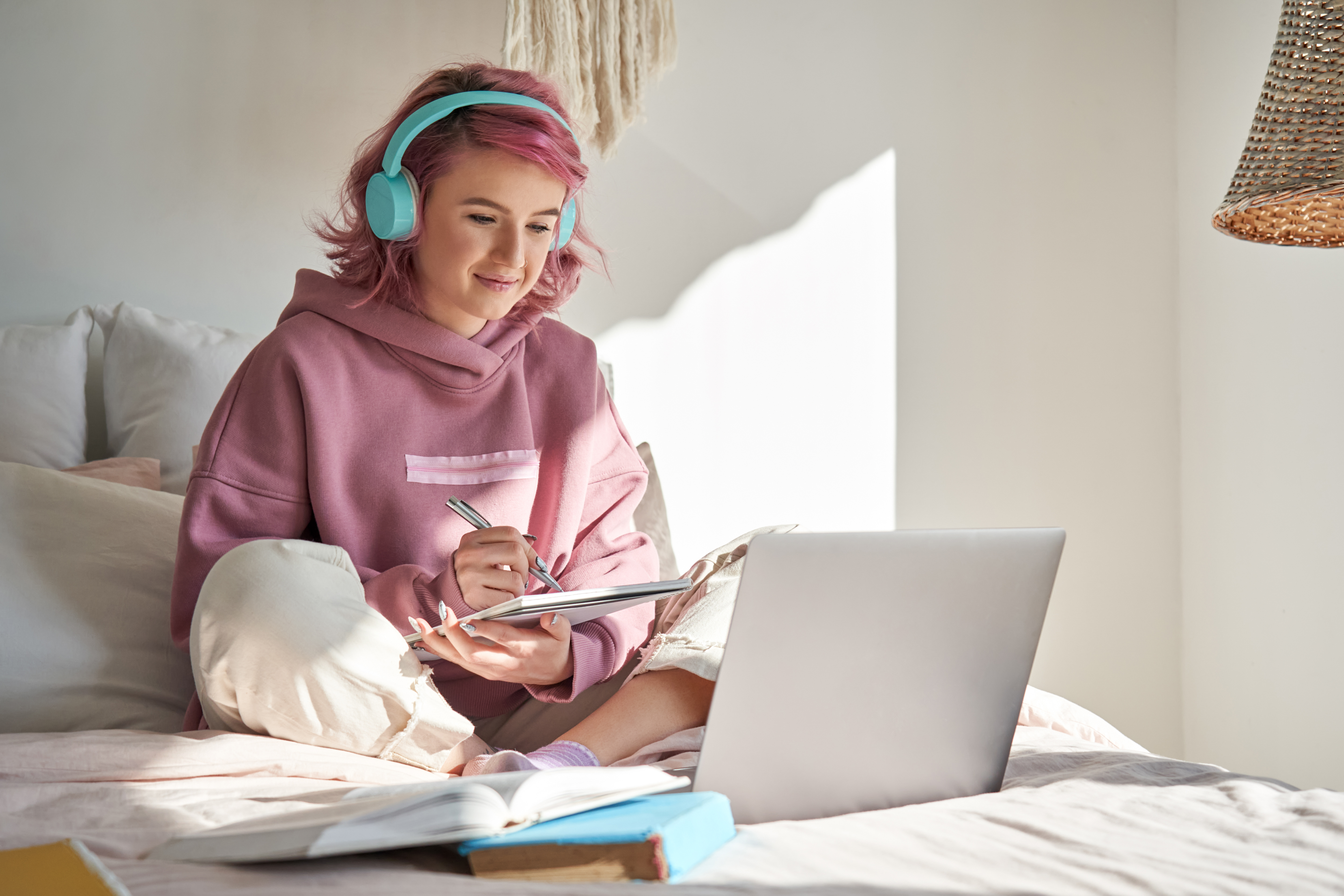 Young woman with headphones on sitting on the bed working on her laptop