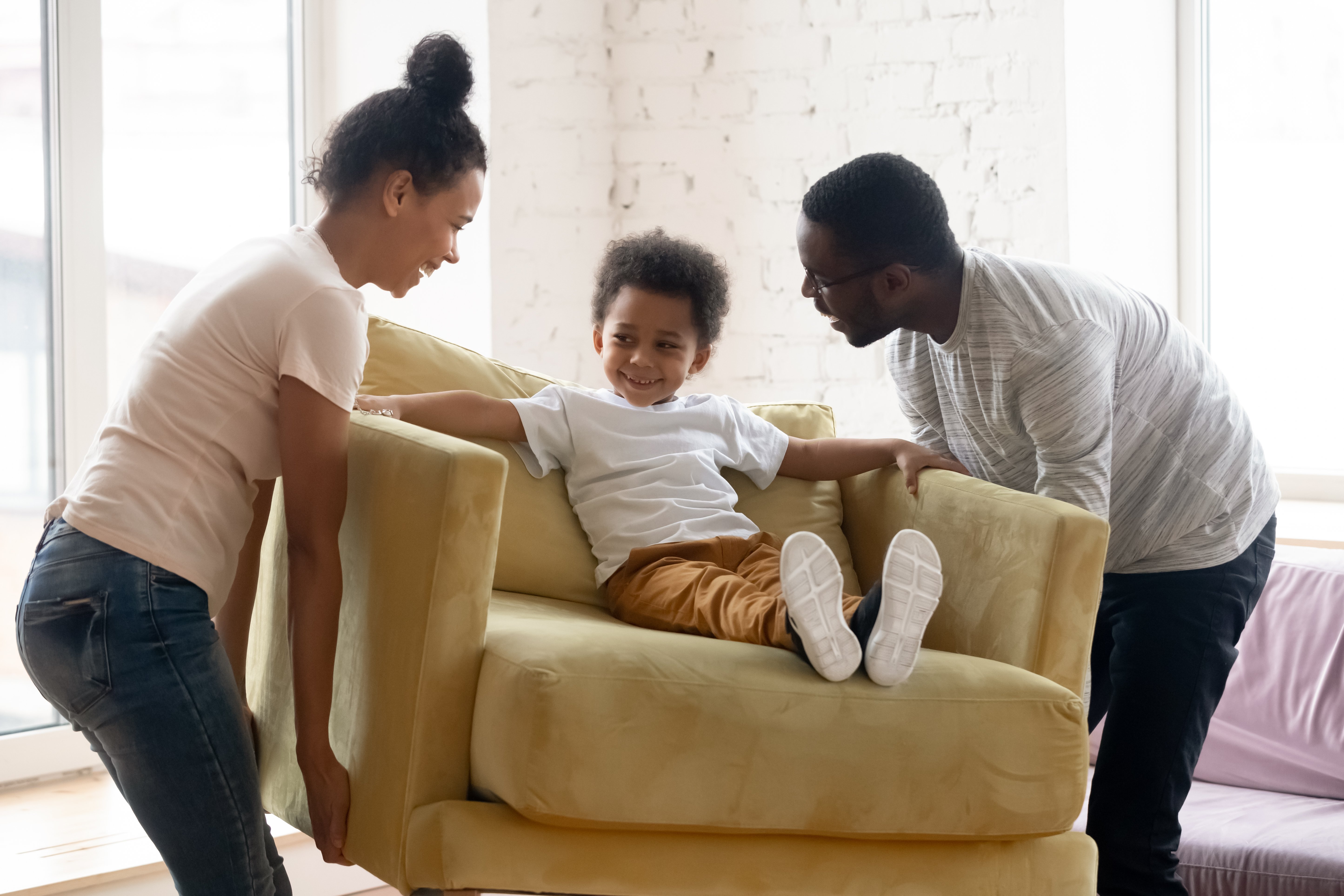 Mother and father moving a chair their son is sitting on