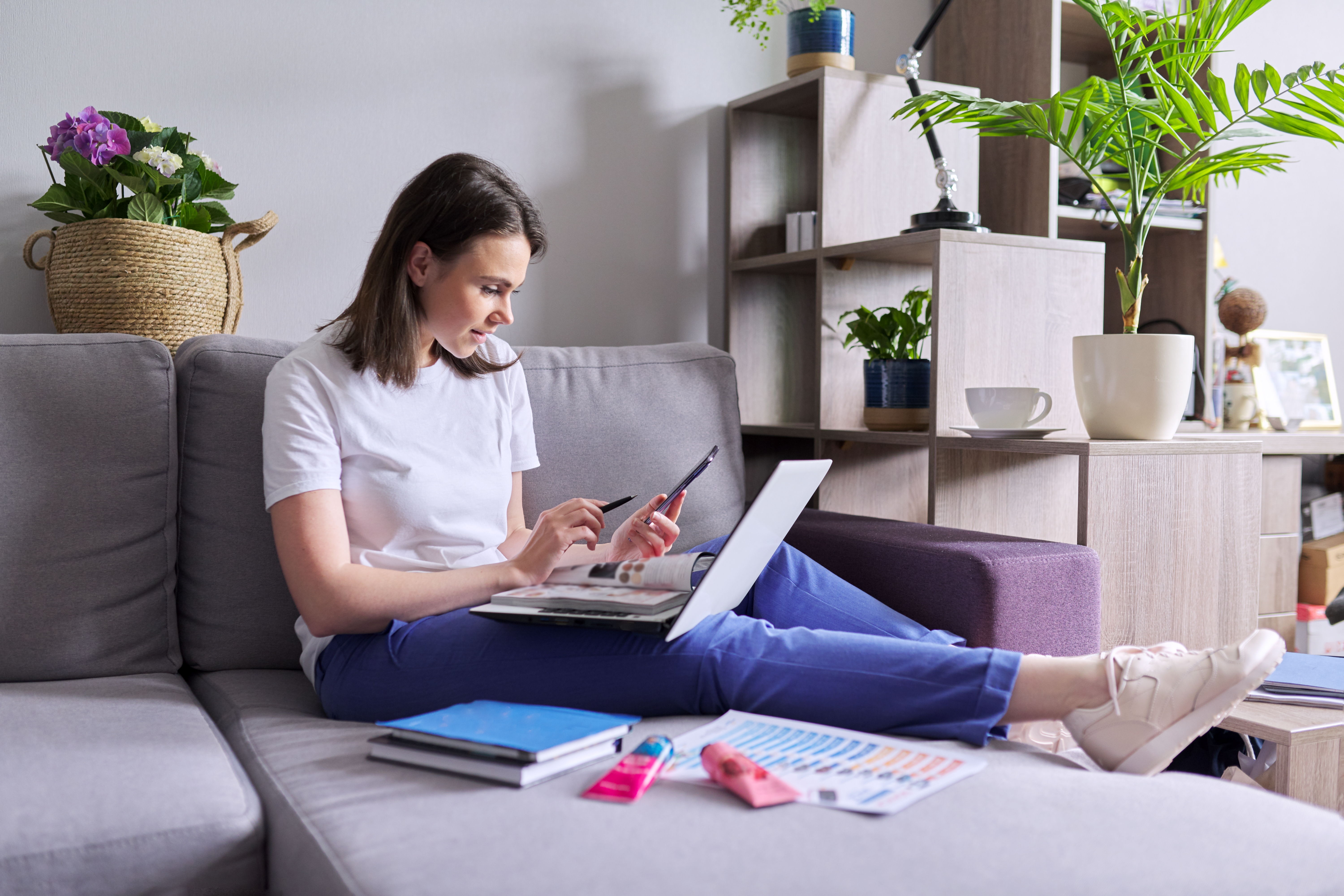 Woman sitting on the couch with her laptop open looking at her phone