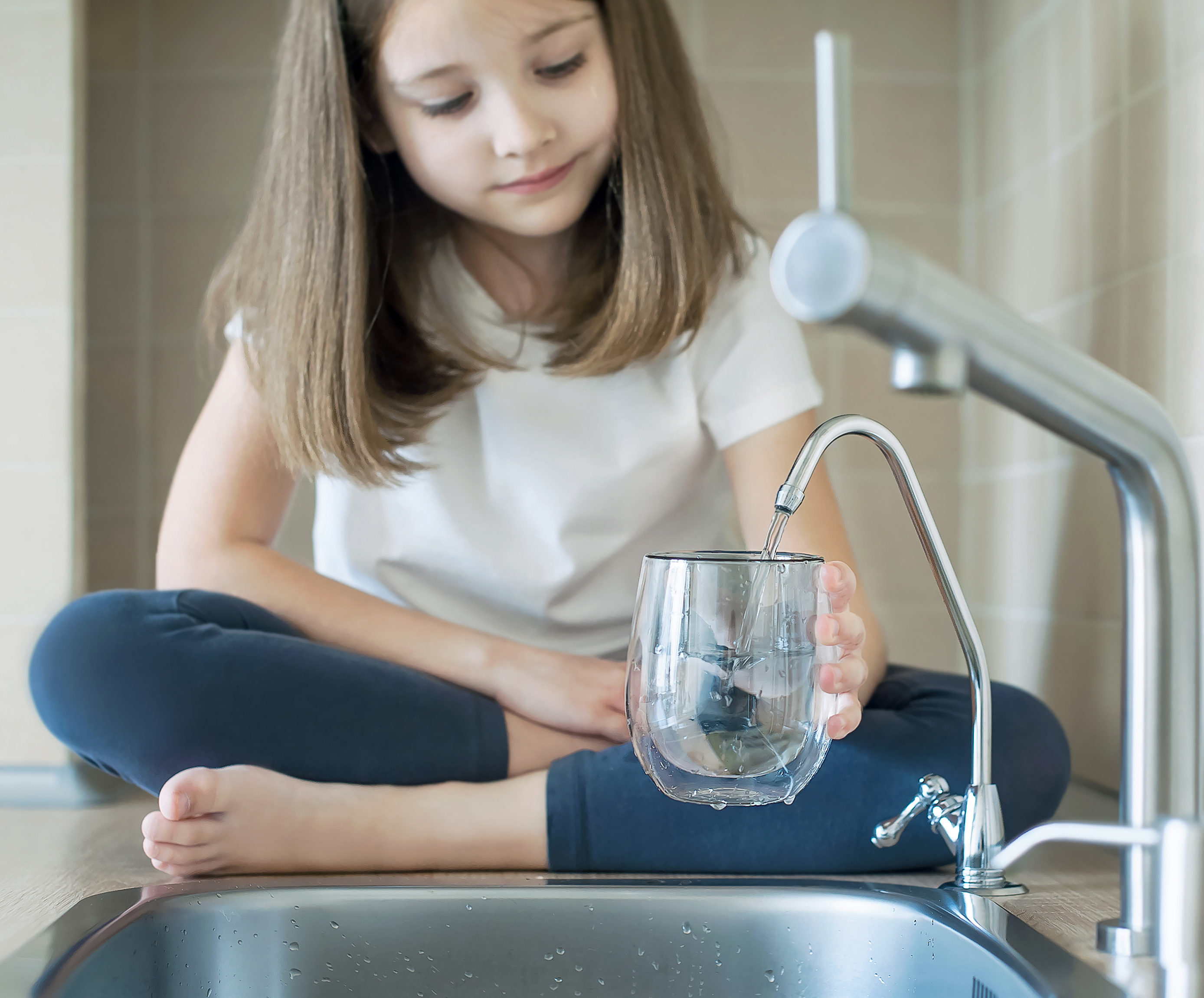 Young girl sitting on the counter filling up a glass of water