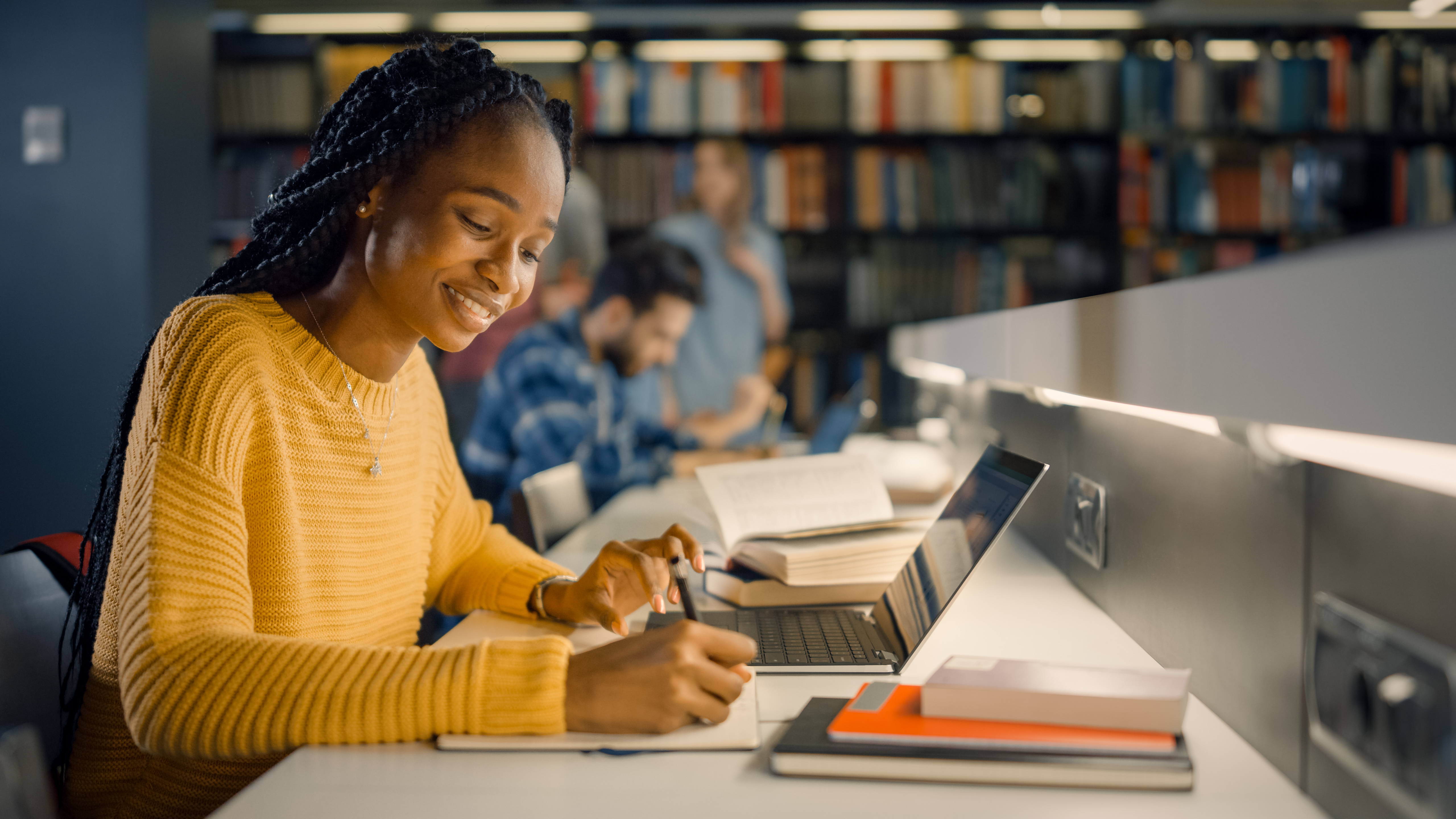 Girl sitting in the library with her laptop open taking notes