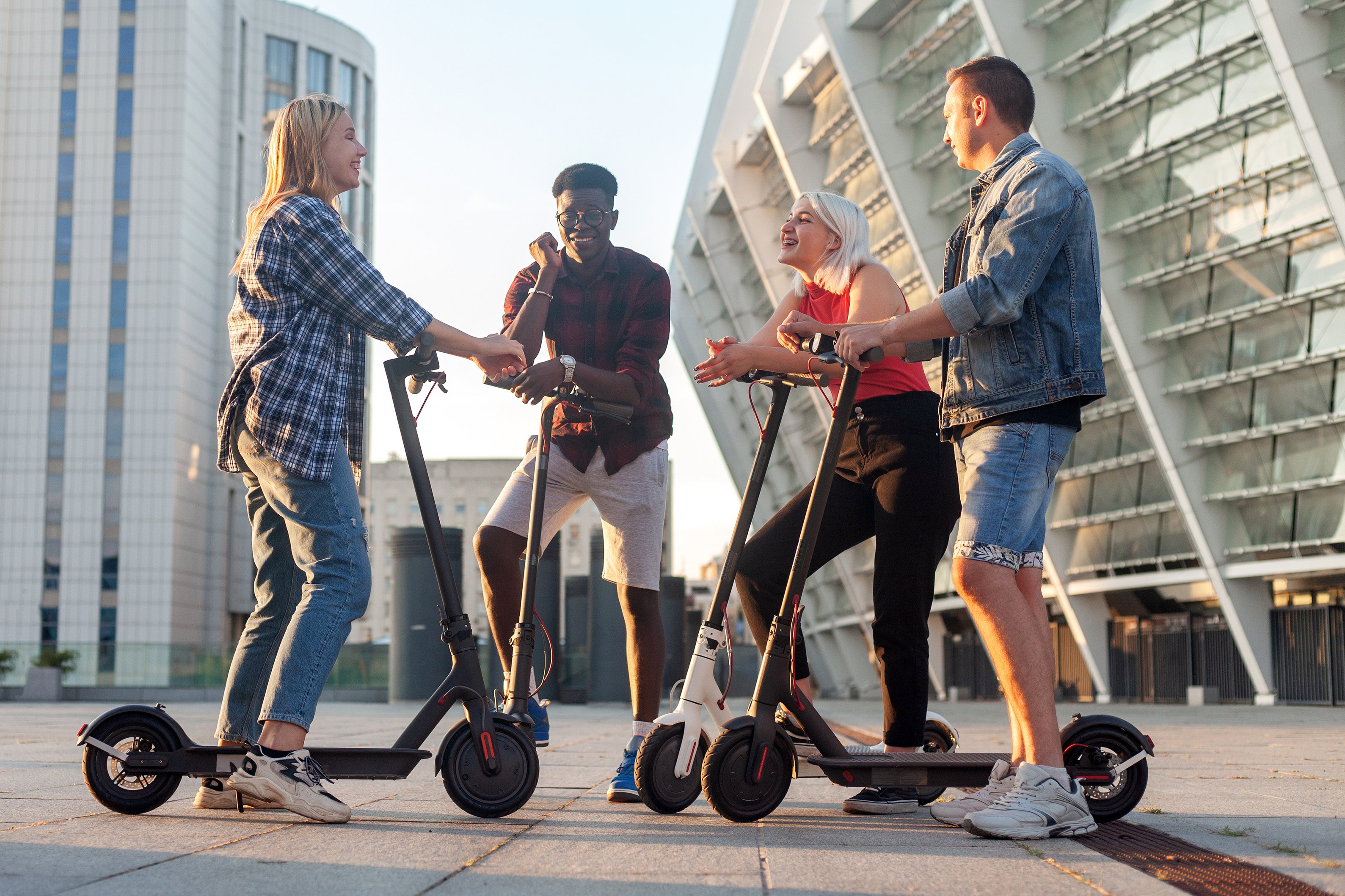 Four people standing outside with electric scooters