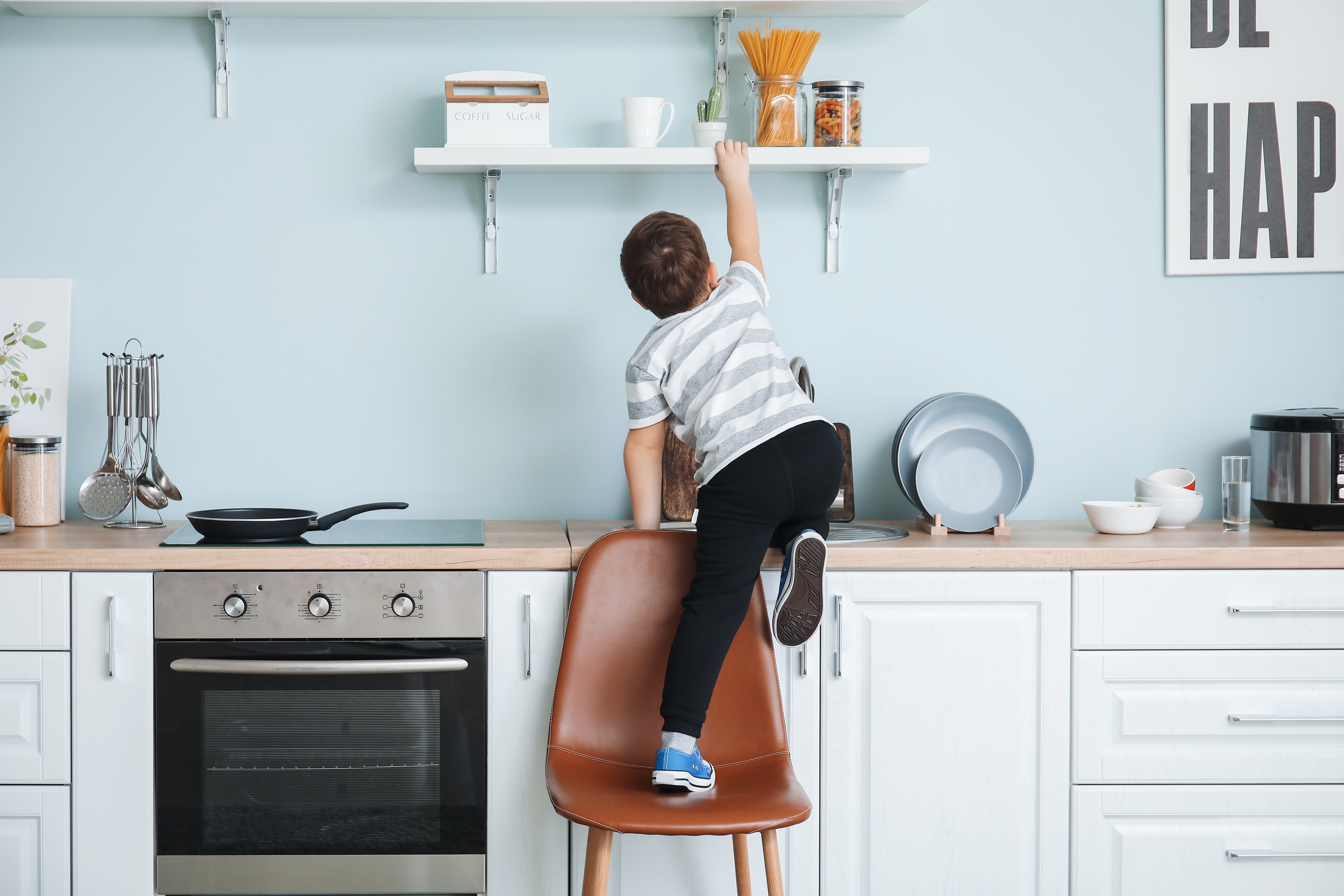 Little boy climbing on a chair to reach something on a shelf