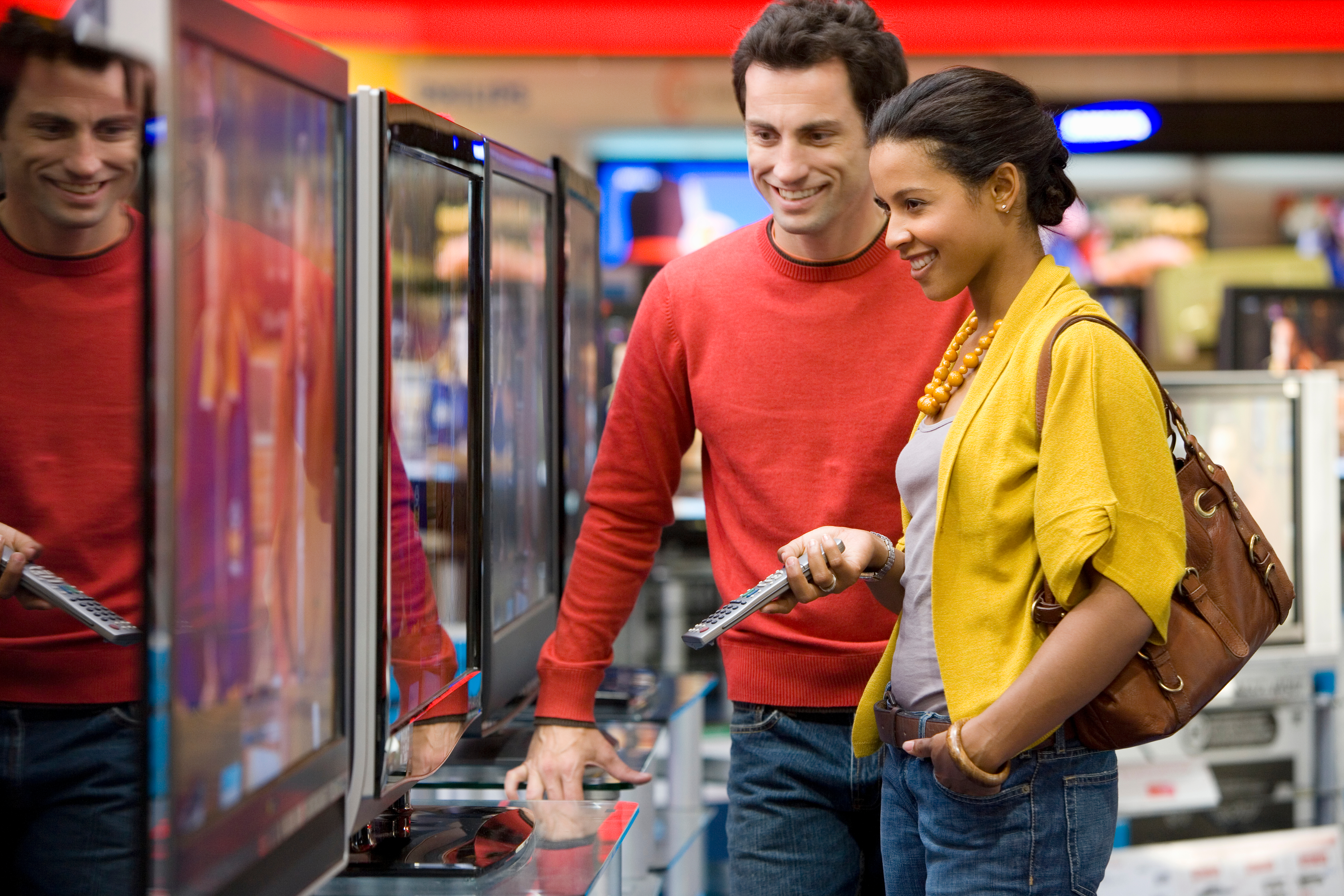 Man in red sweater and woman in yellow jacket shopping for a TV