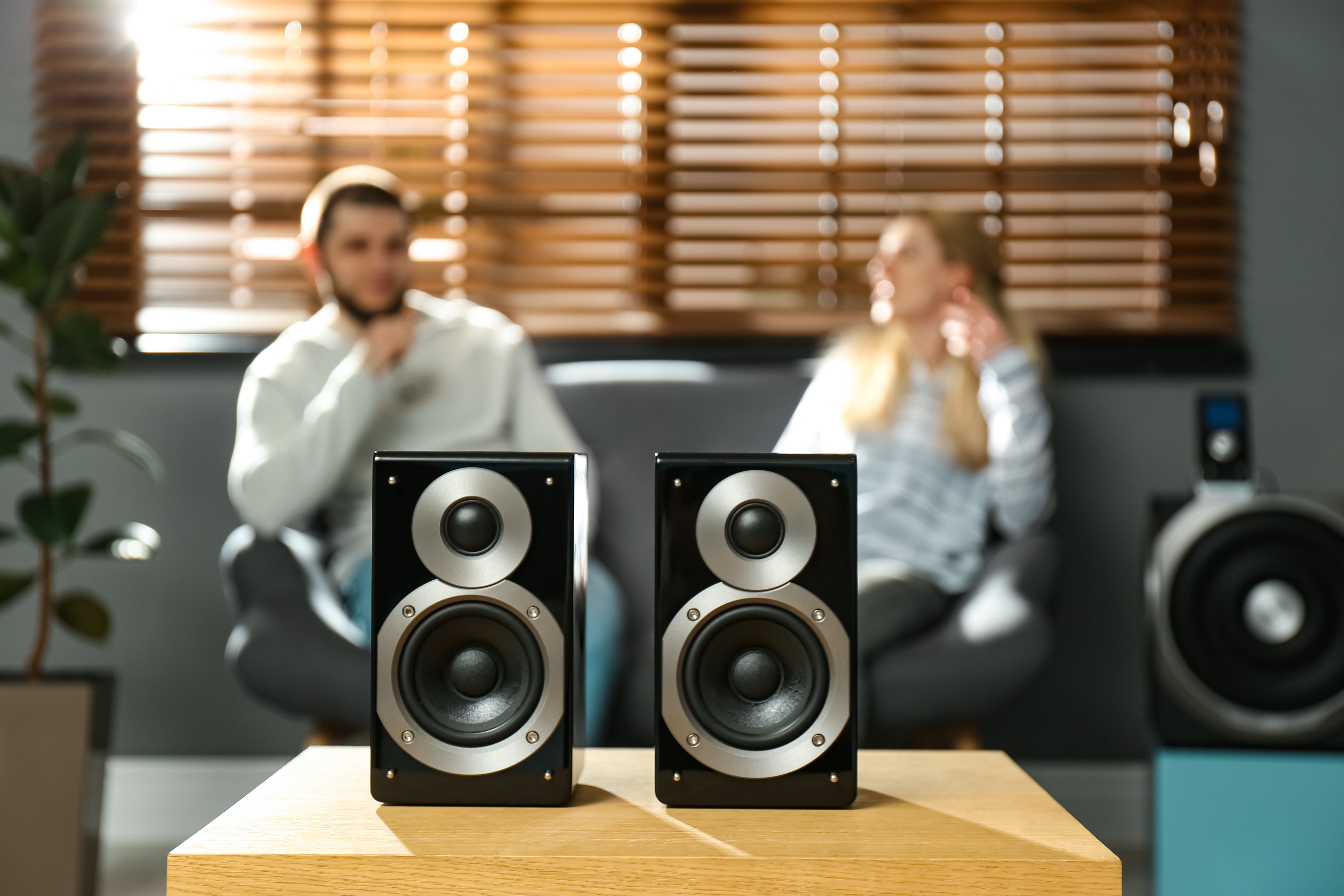 Man and woman sitting on couch with two speakers in the foreground