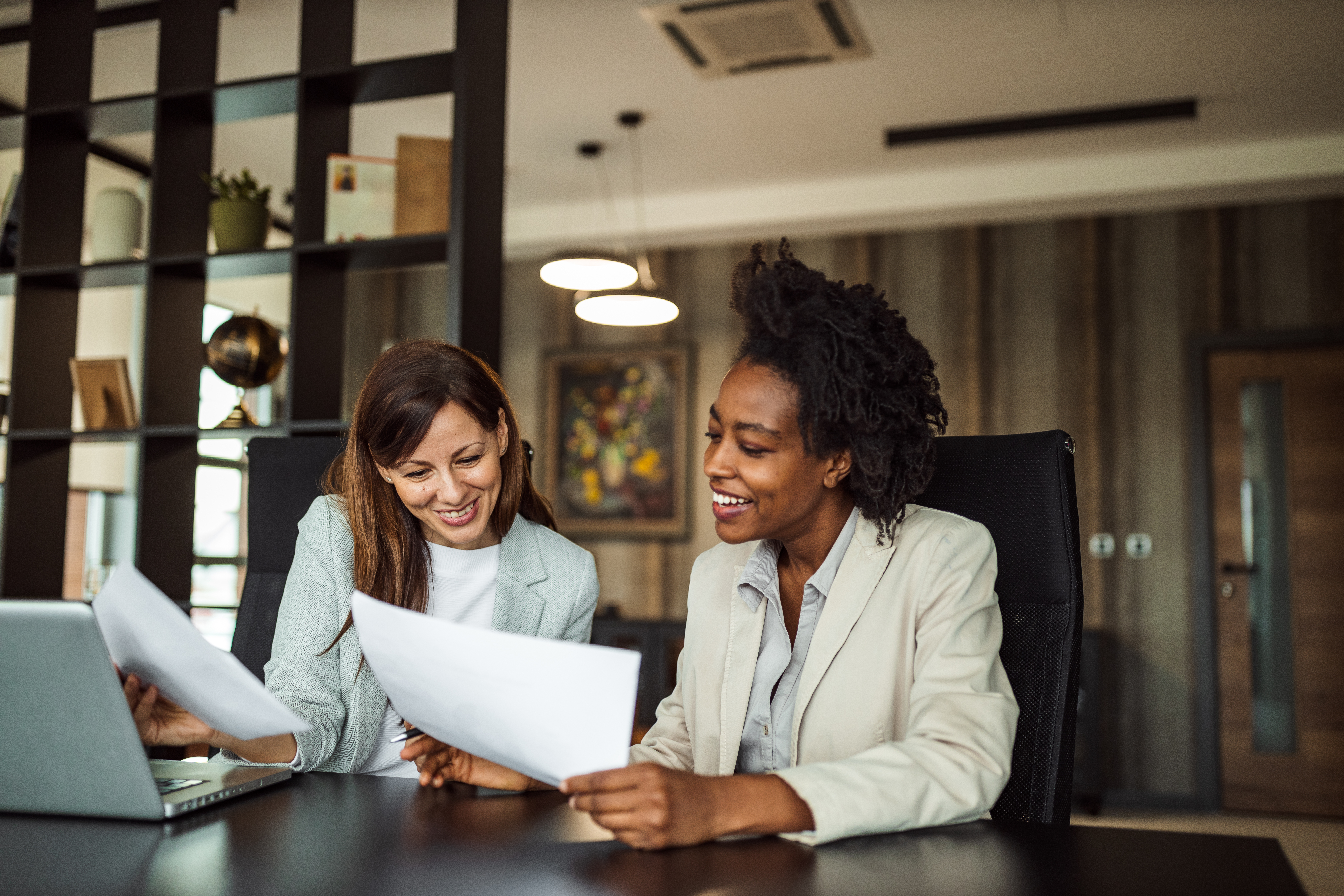 Two woman sitting at a desk looking at papers