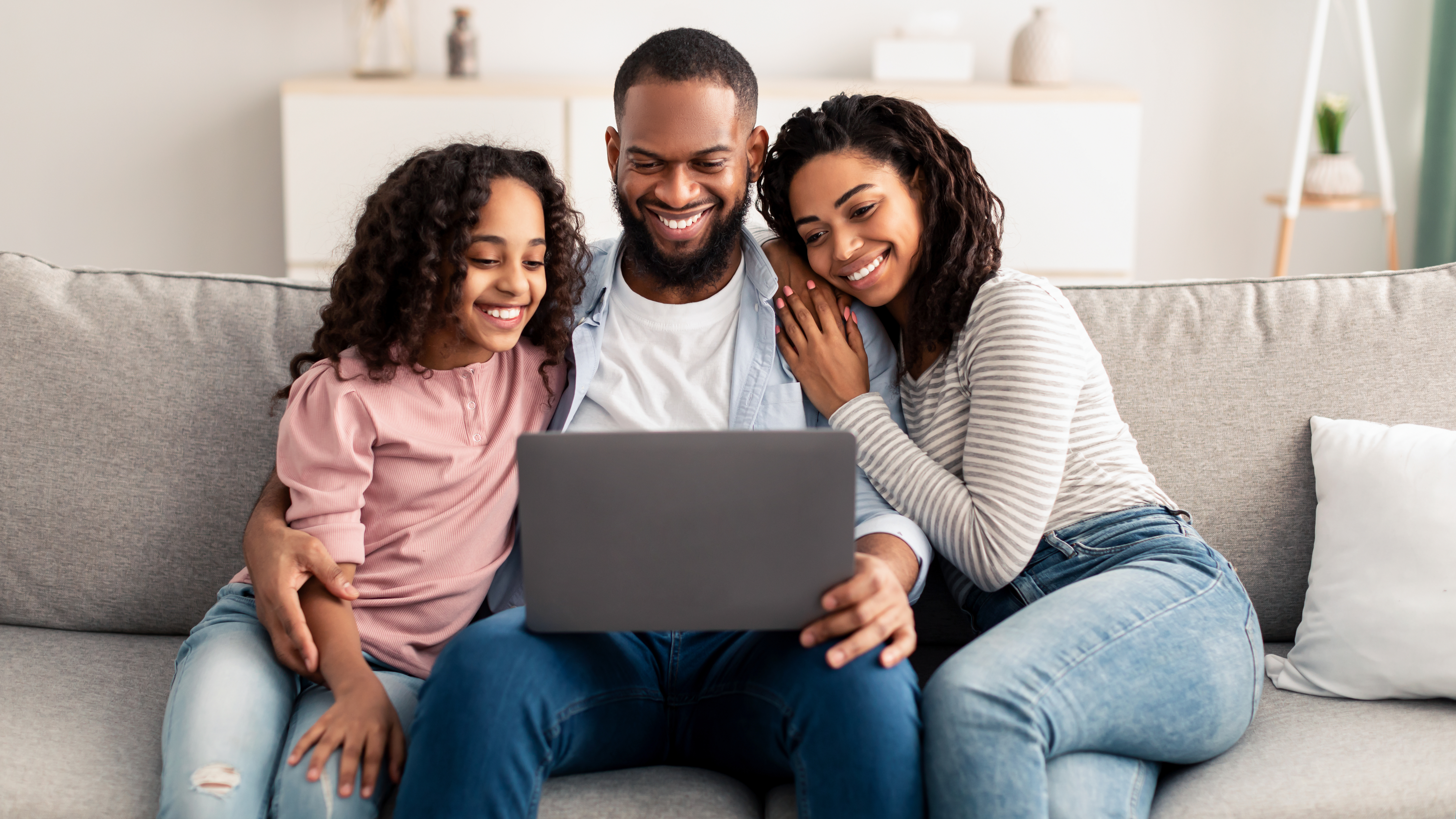 Father sitting on the couch with his two daughters looking at a laptop