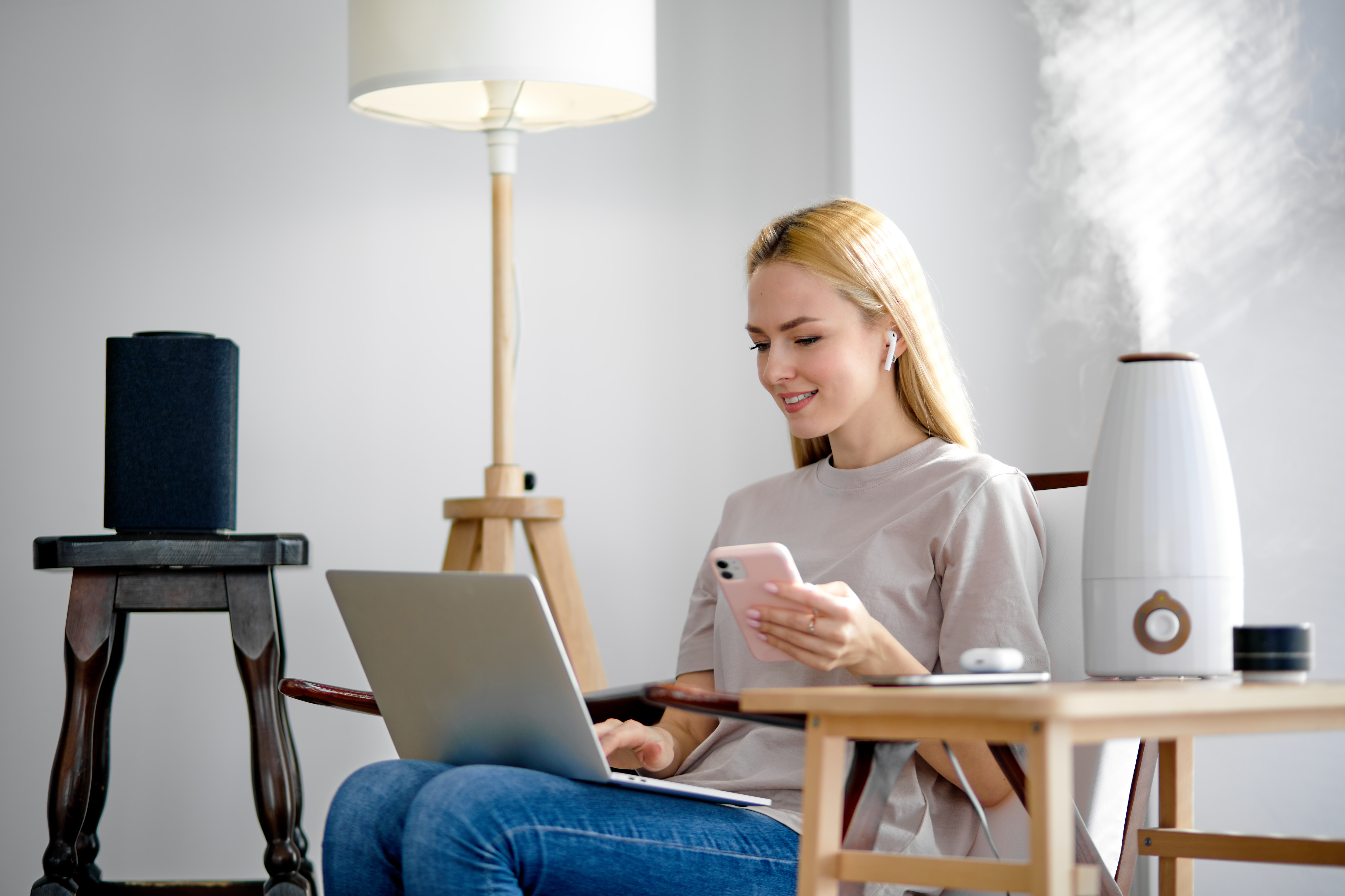 Woman sitting in a chair on her smartphone and laptop with a humidifier going