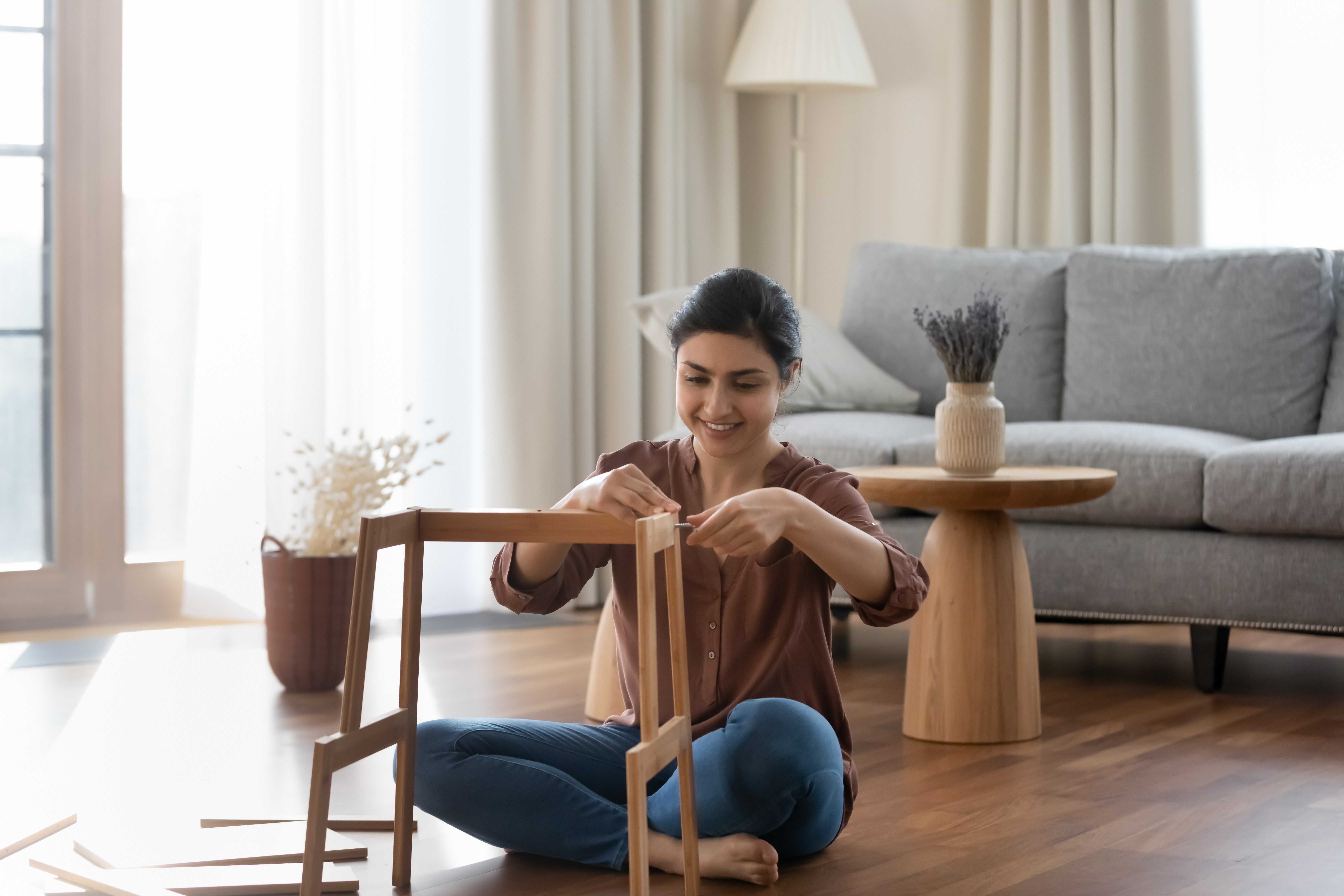 Woman wearing brown shirt sitting on floor assembling a chair