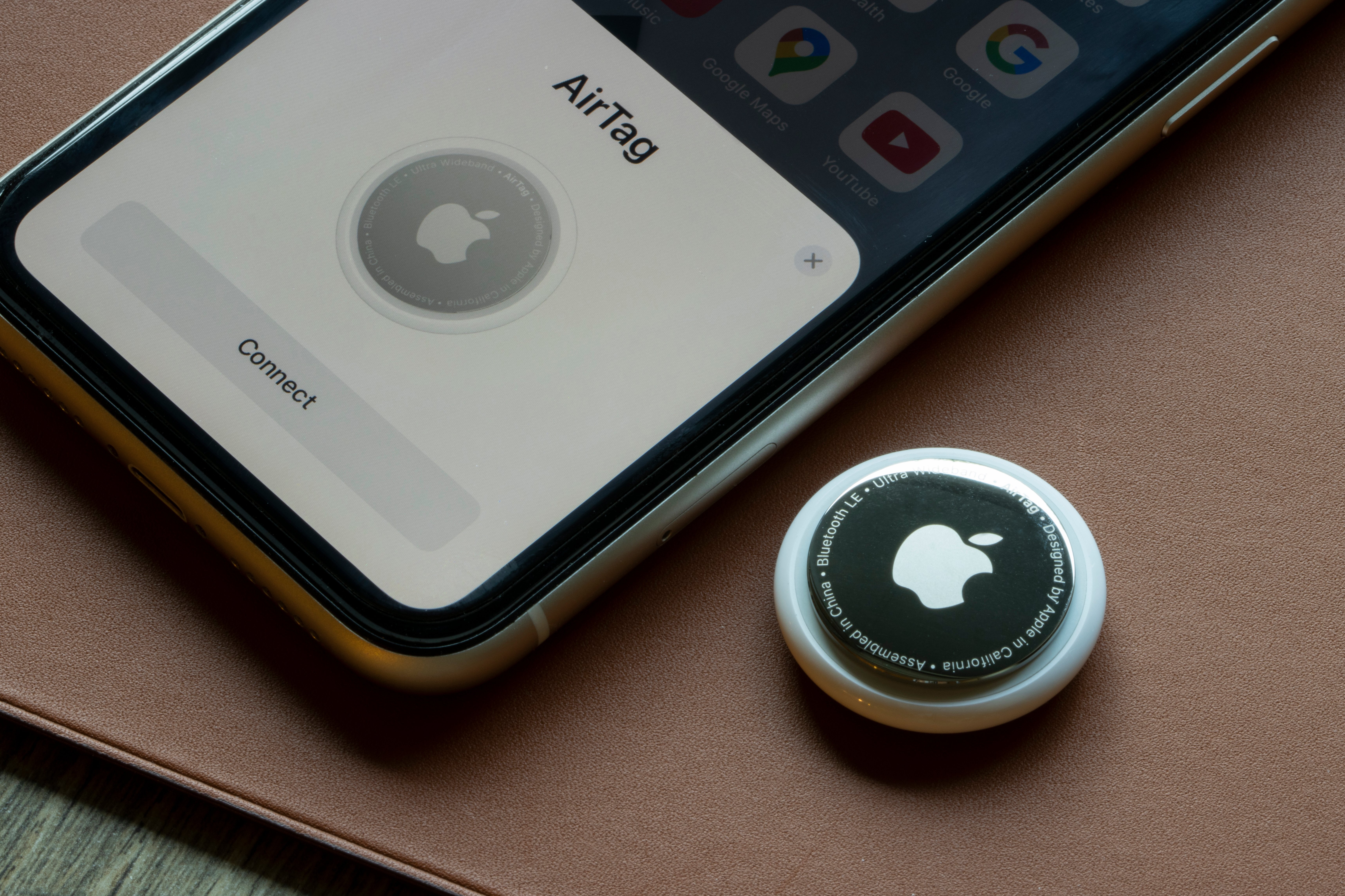 Apple AirTag and Apple iPhone on table next to each other