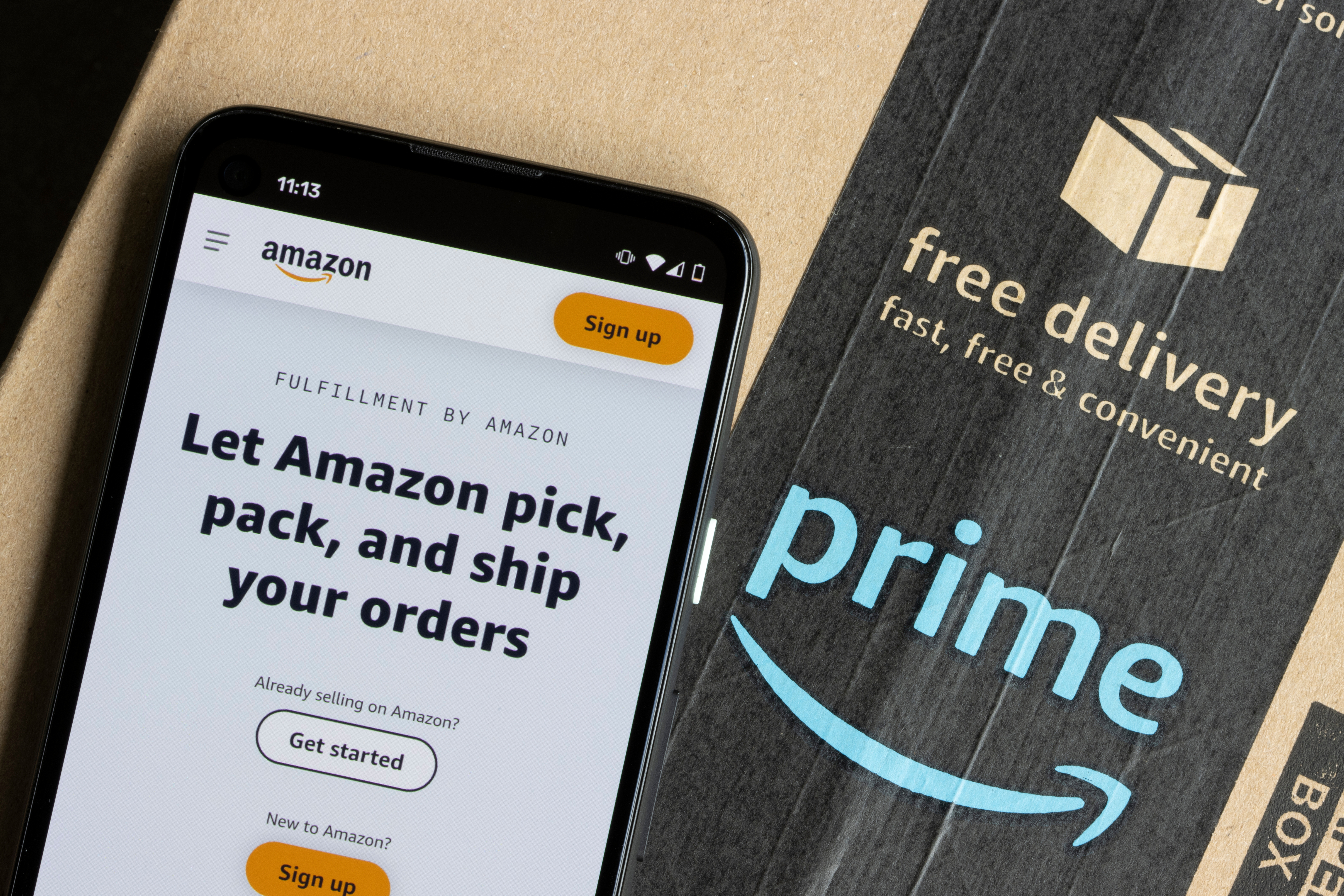 Smartphone with the Amazon logo on it next to an Amazon shipping box