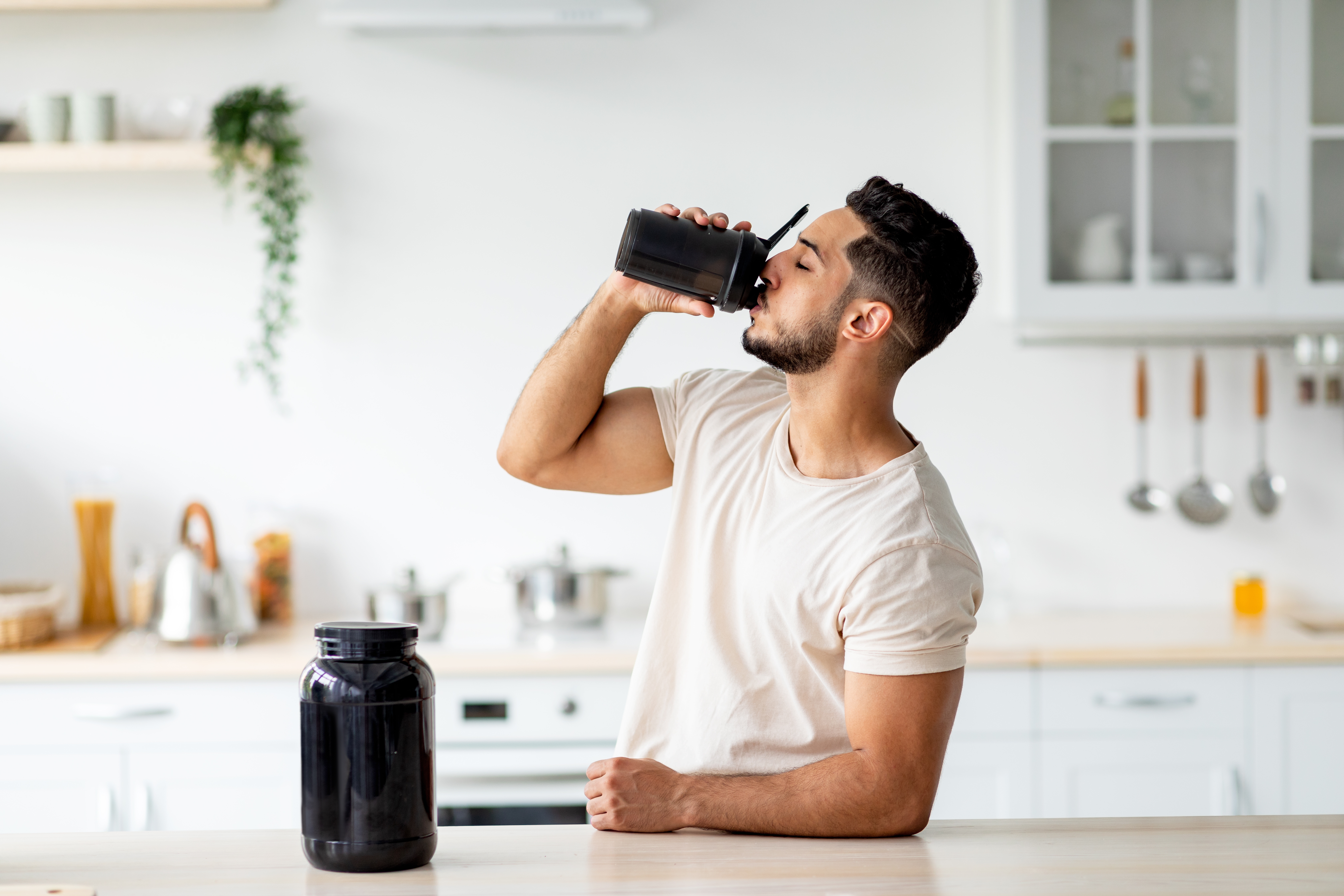 Man standing at kitchen counter drinking a protein shake