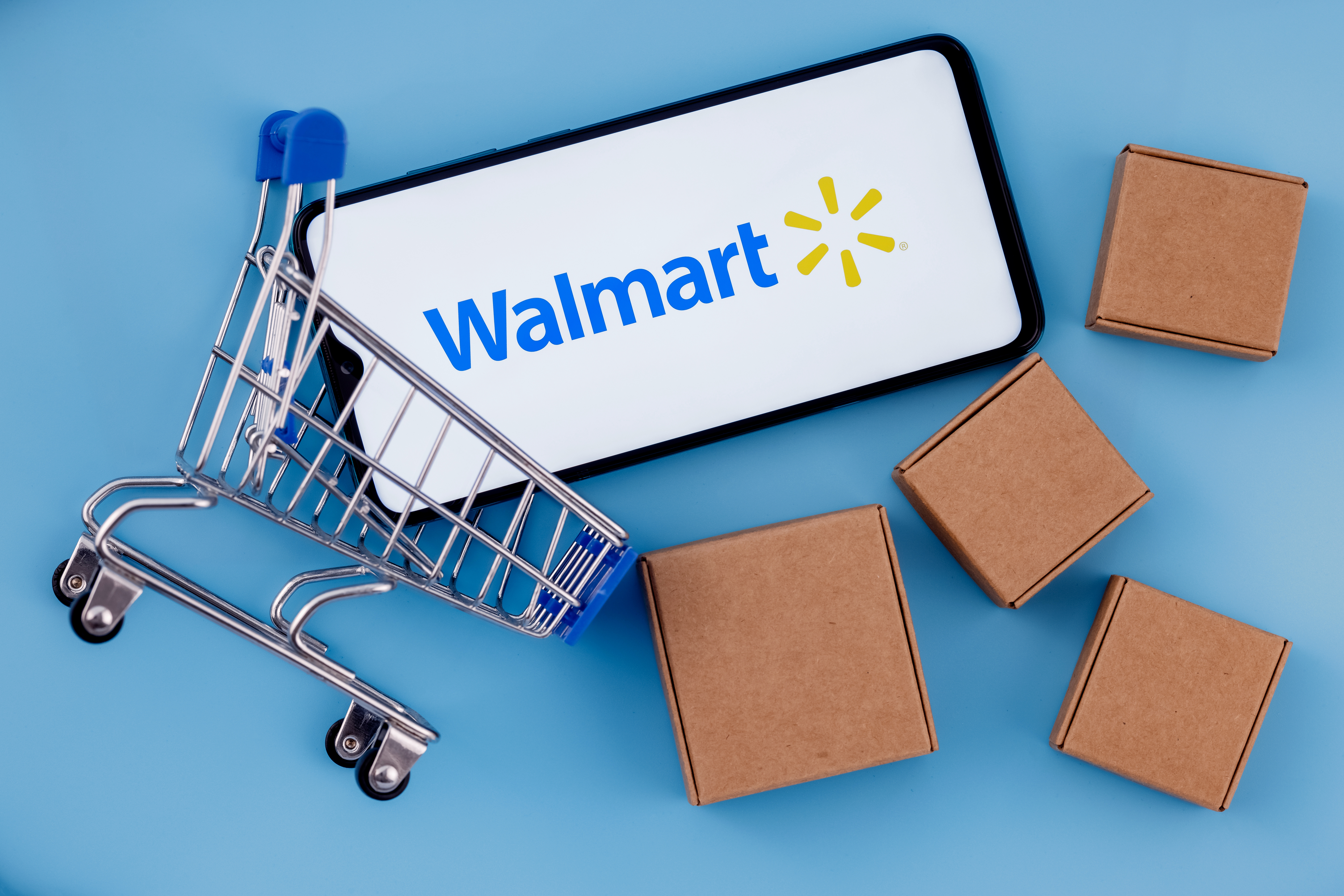 Smartphone with the Walmart logo on it in a small shopping cart next to cardboard boxes