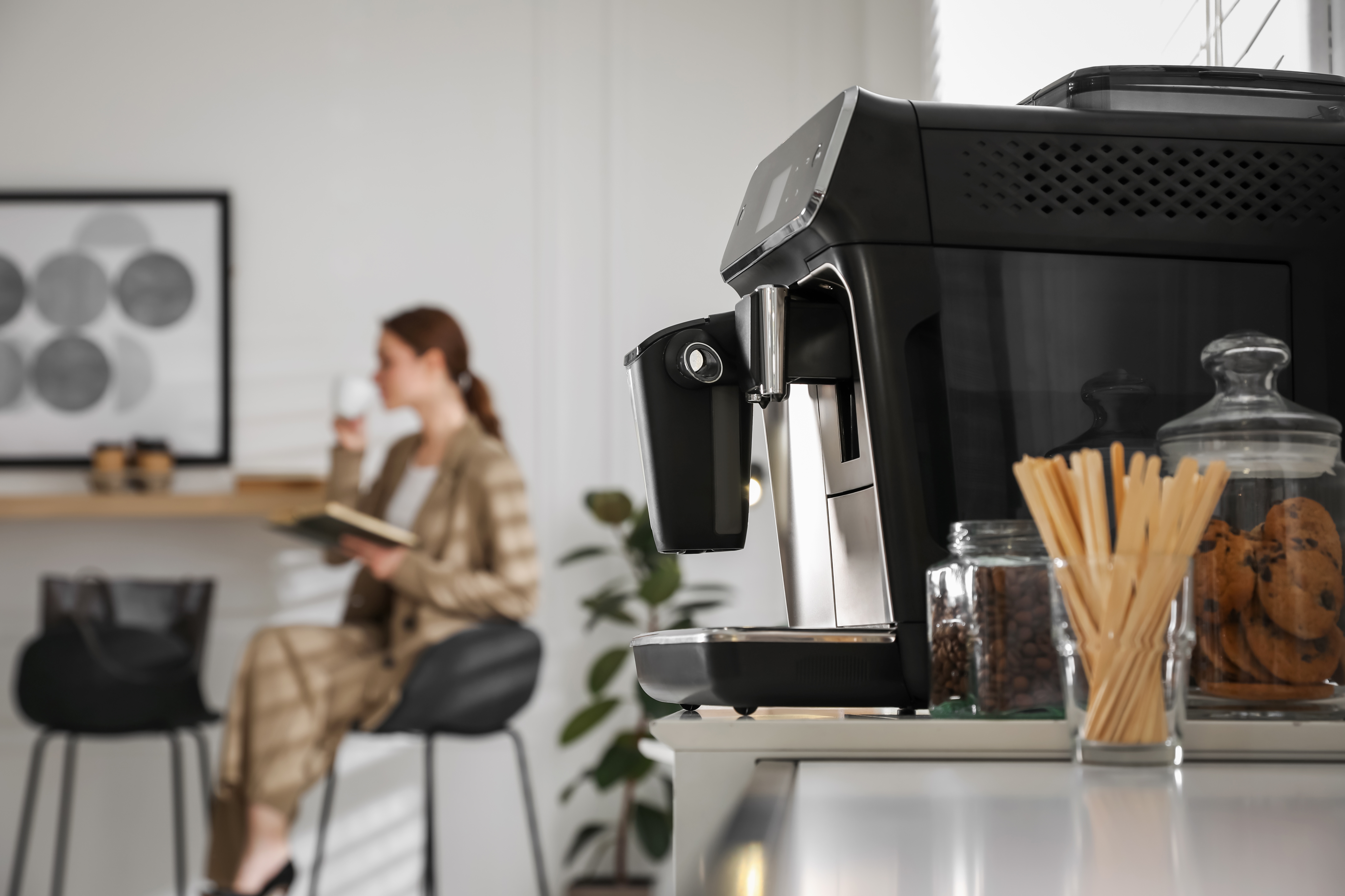 Woman sitting in the kitchen with an espresso maker in the foreground