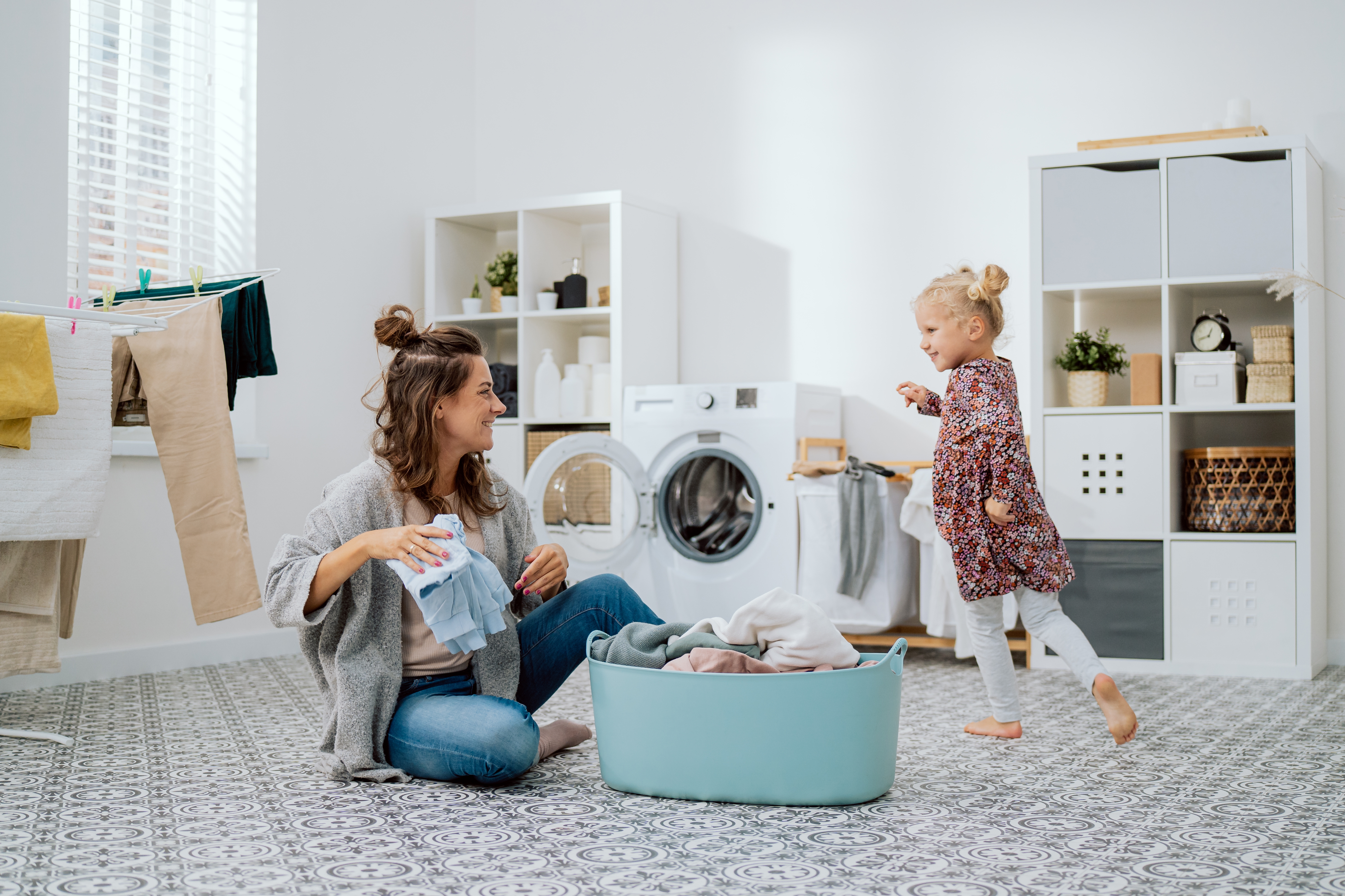 Mother doing laundry in the laundry room while daughter runs around