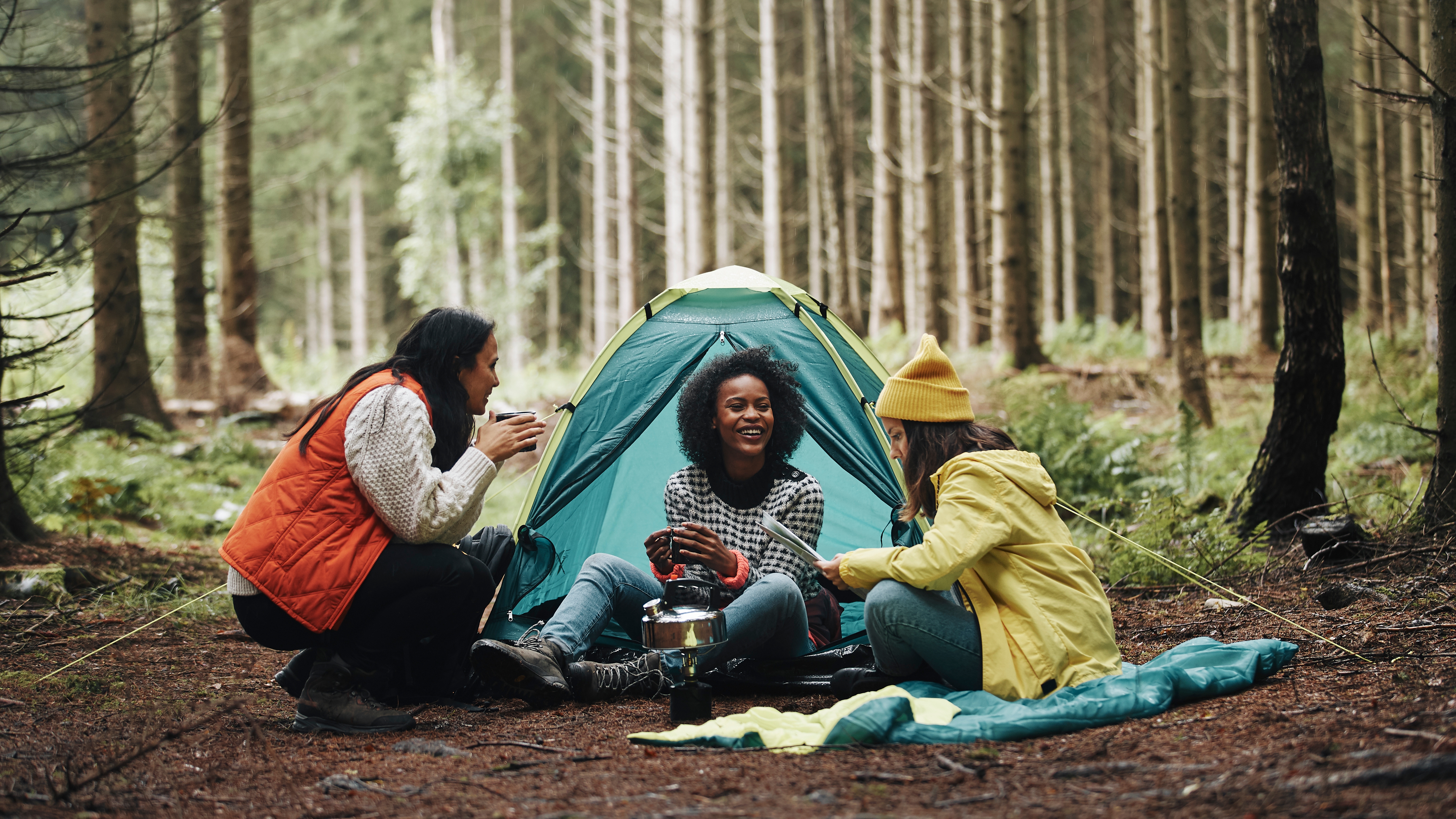 Three women sitting outside of a tent while camping