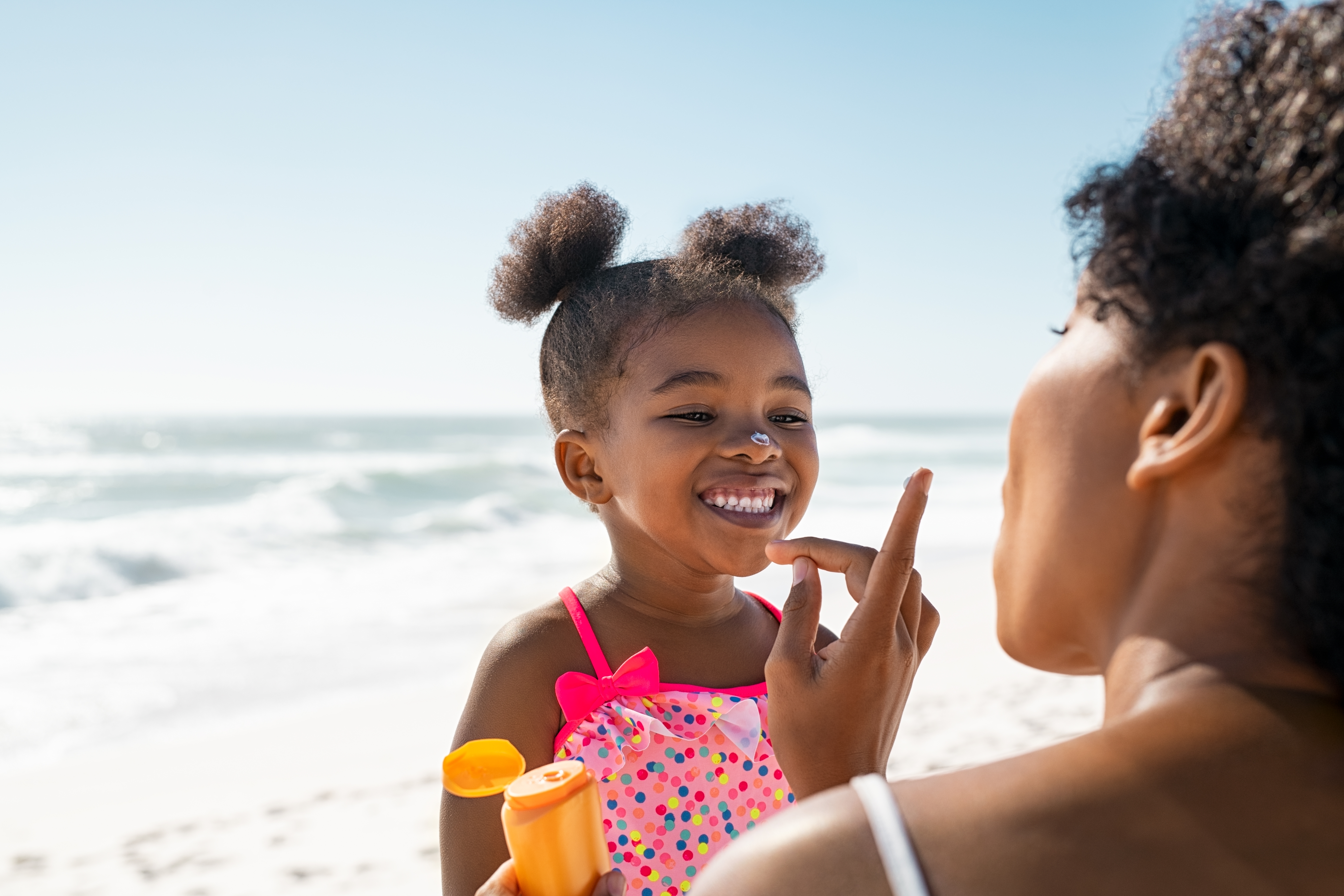 Mom applying sunscreen to her daughter's face at the beach